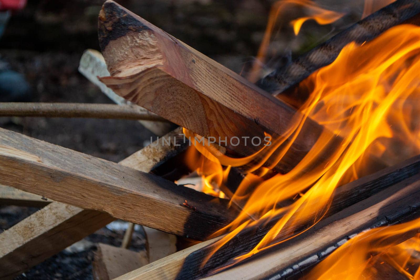 A fire burns in a campfire with a red fire in the background. High quality photo