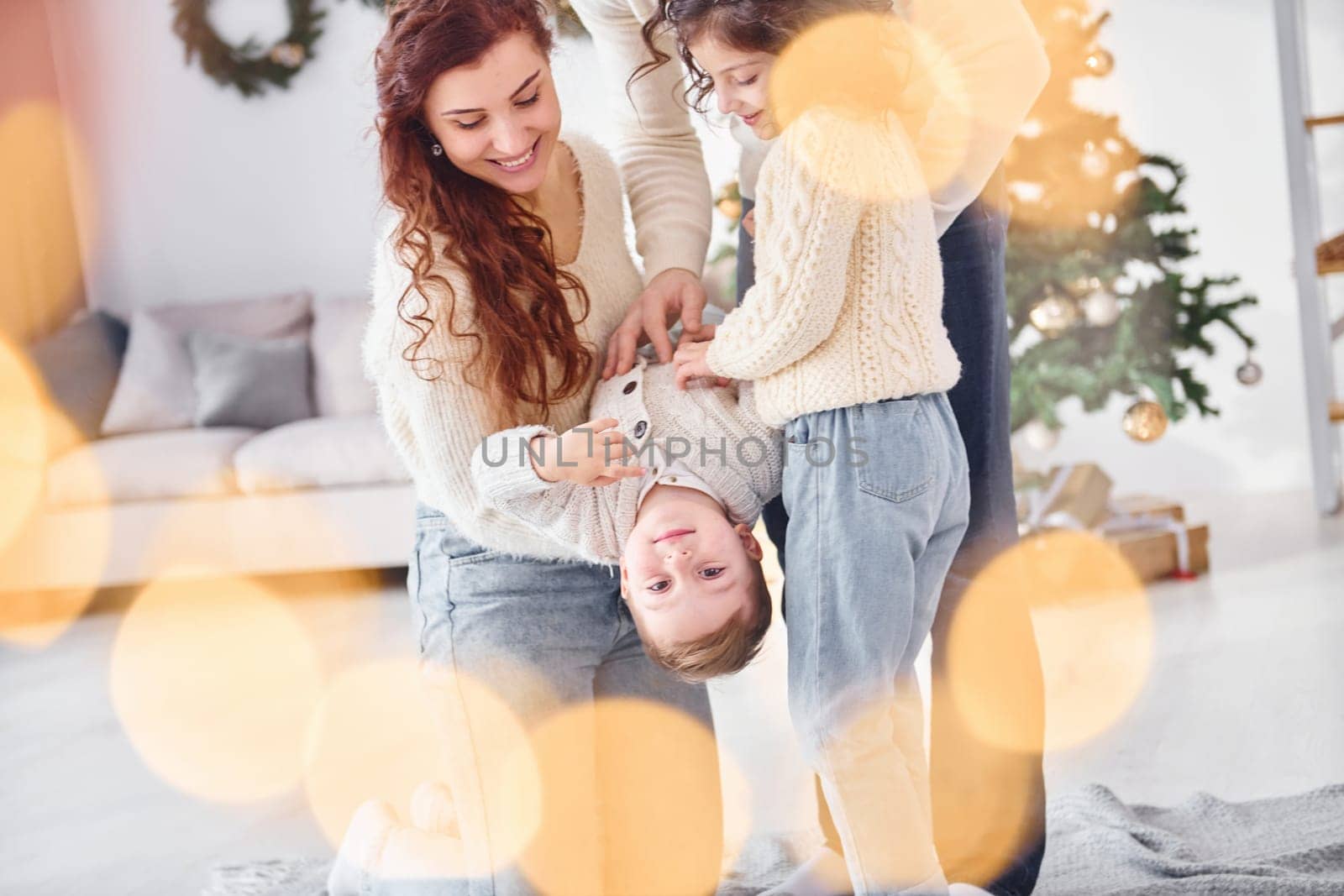 Standing in the domestic room and holding boy in hands. Family celebrating new year with their children at home.
