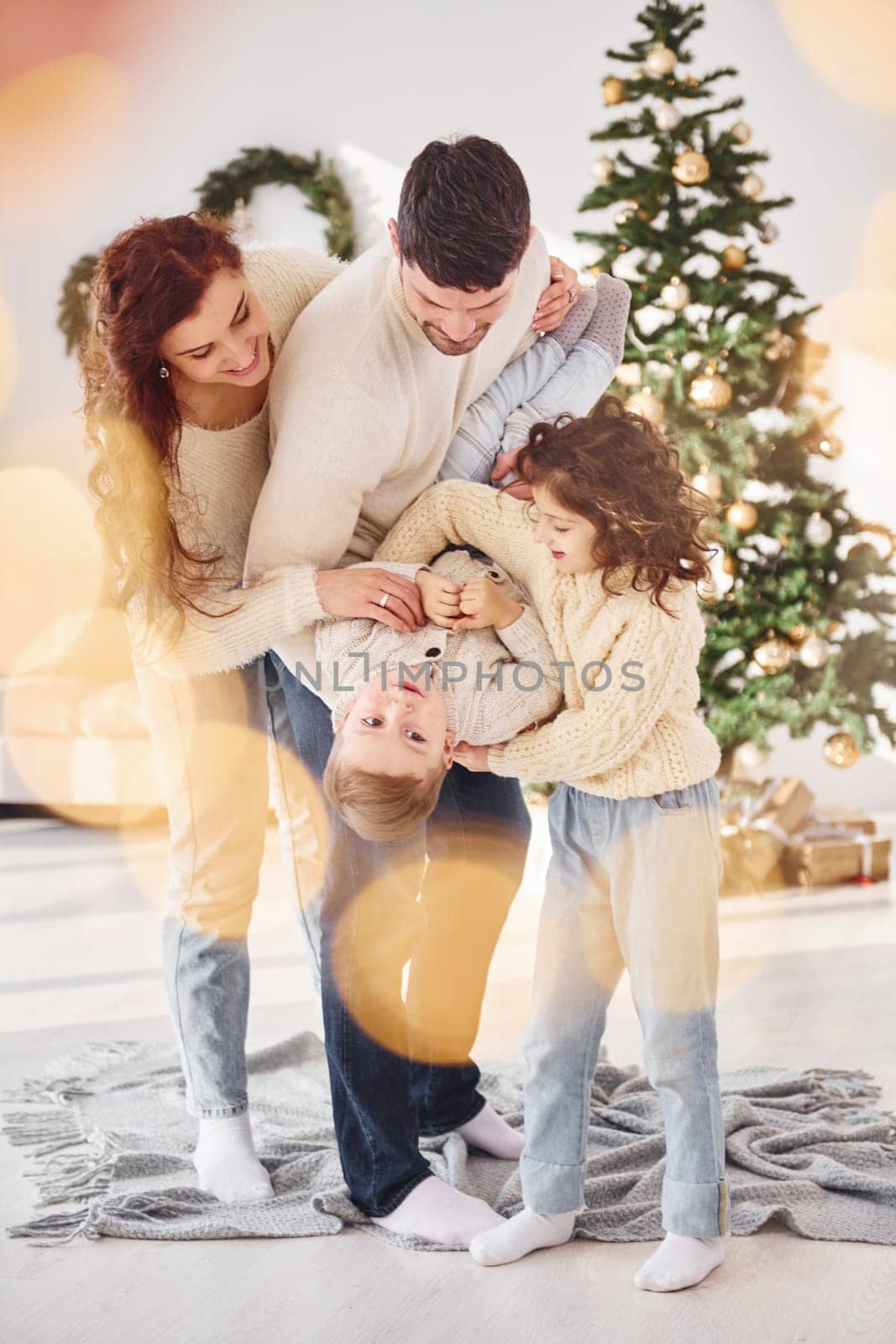 Standing in the domestic room and holding boy in hands. Family celebrating new year with their children at home.