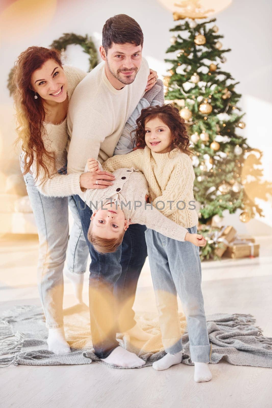 Standing in the domestic room and holding boy in hands. Family celebrating new year with their children at home.