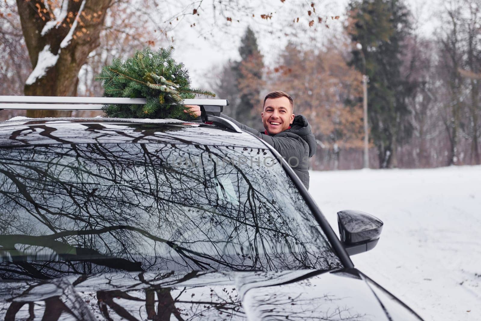 Preparing for the weekend. Man with little green fir is outdoors near his car. Conception of holidays.