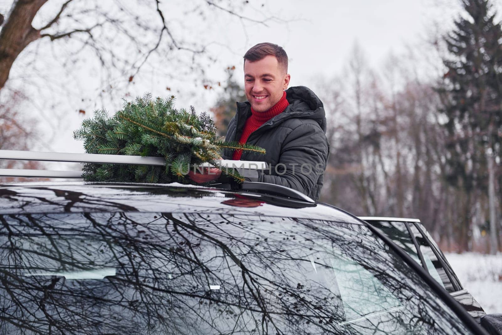 Preparing for the weekend. Man with little green fir is outdoors near his car. Conception of holidays.