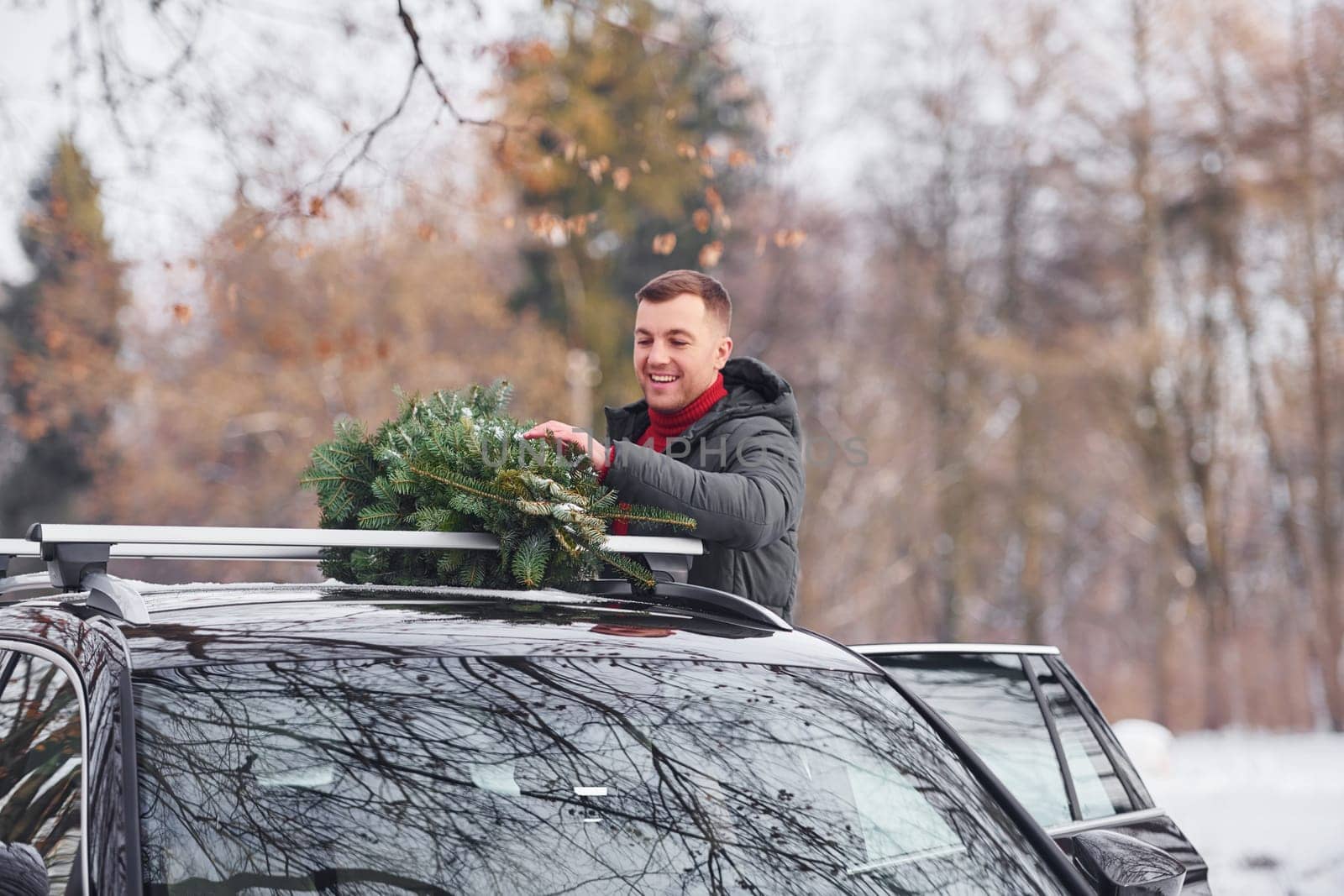 In the forest. Man with little green fir is outdoors near his car. Conception of holidays.