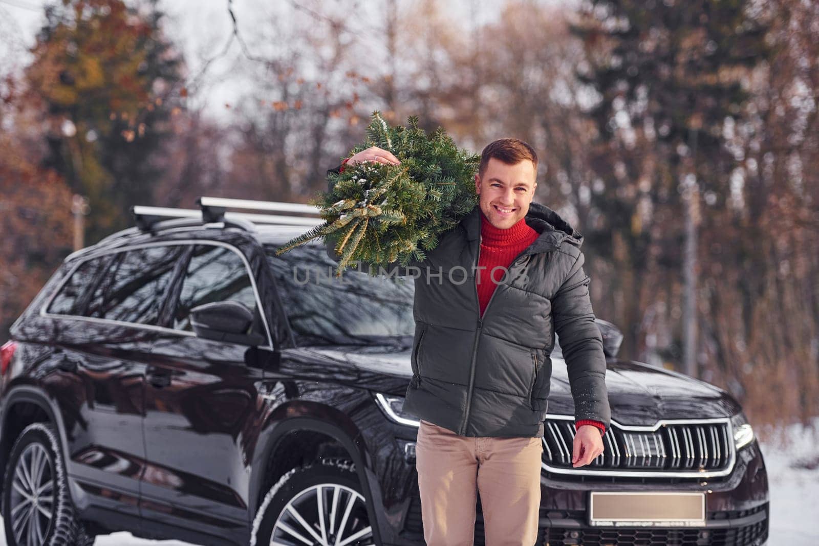 In the forest. Man with little green fir is outdoors near his car. Conception of holidays.