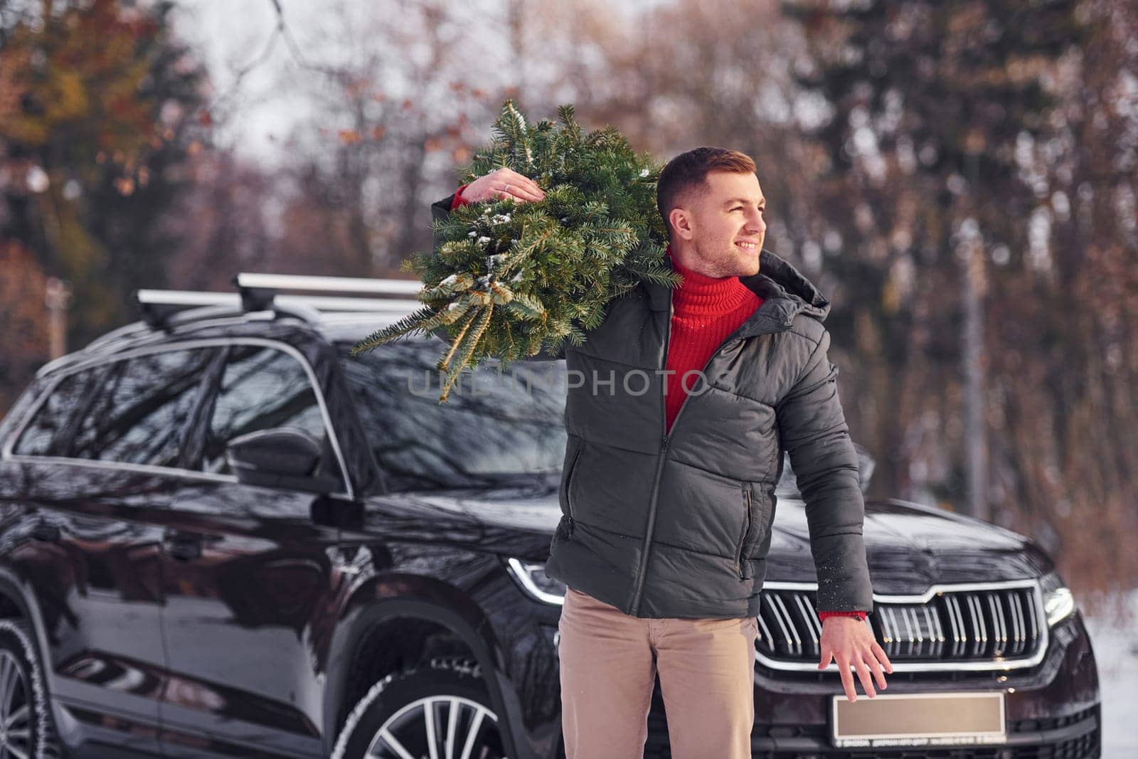 Holding green fir in hands. Man is outdoors near his car. Conception of holidays.