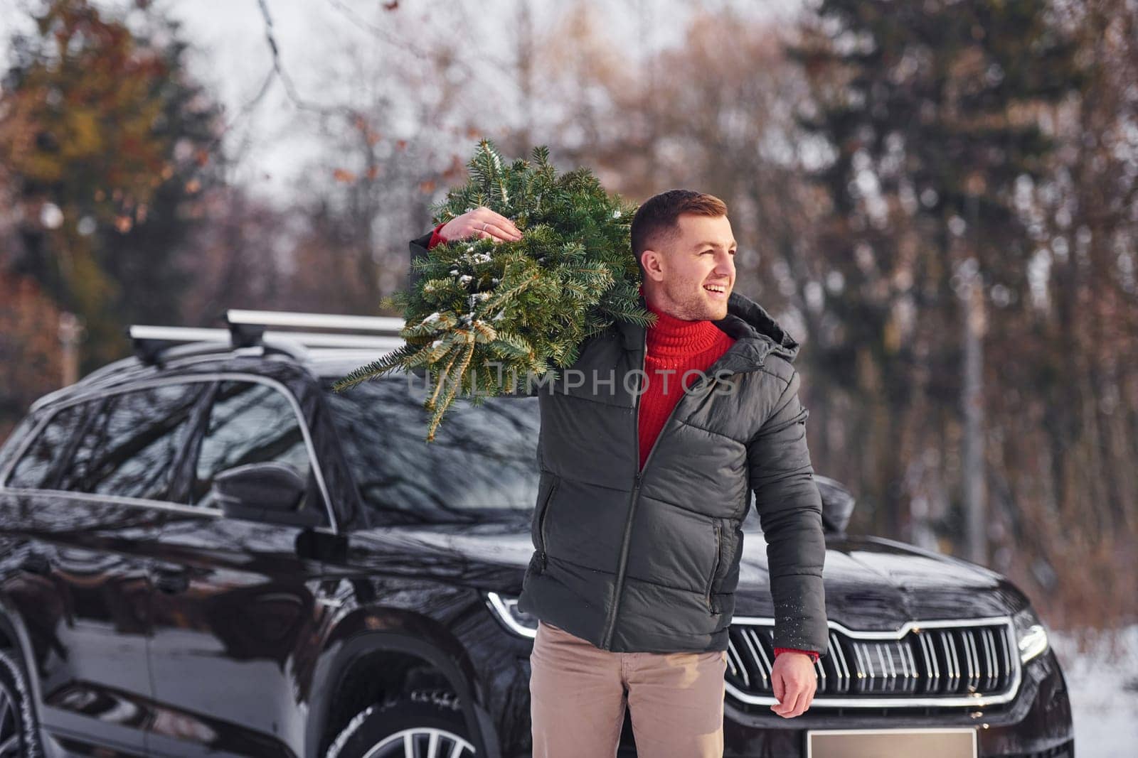 Holding green fir in hands. Man is outdoors near his car. Conception of holidays.