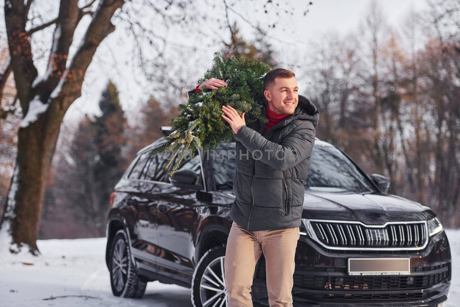 Front view. Man with little green fir is outdoors near his car. Conception of holidays.