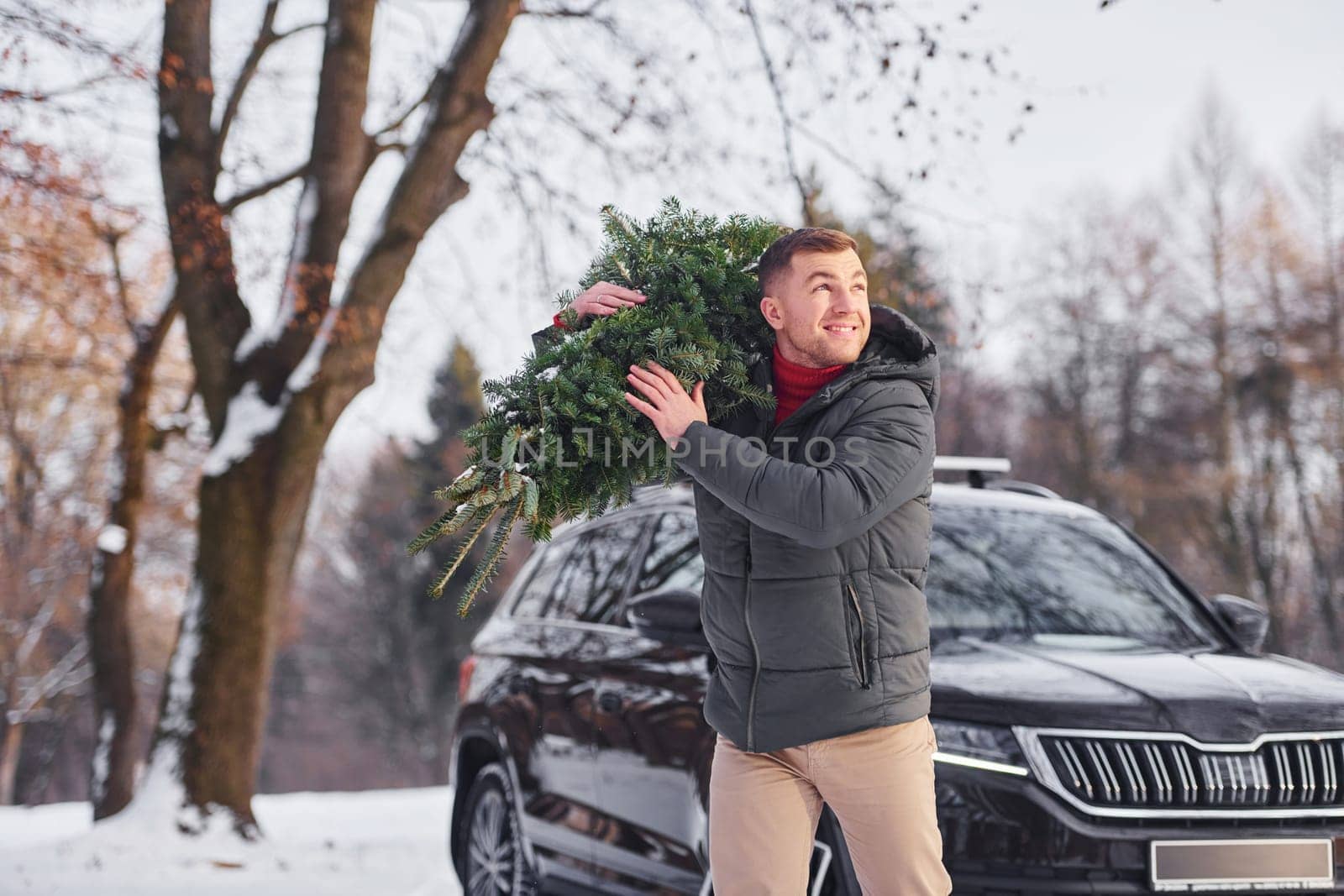 Front view. Man with little green fir is outdoors near his car. Conception of holidays.