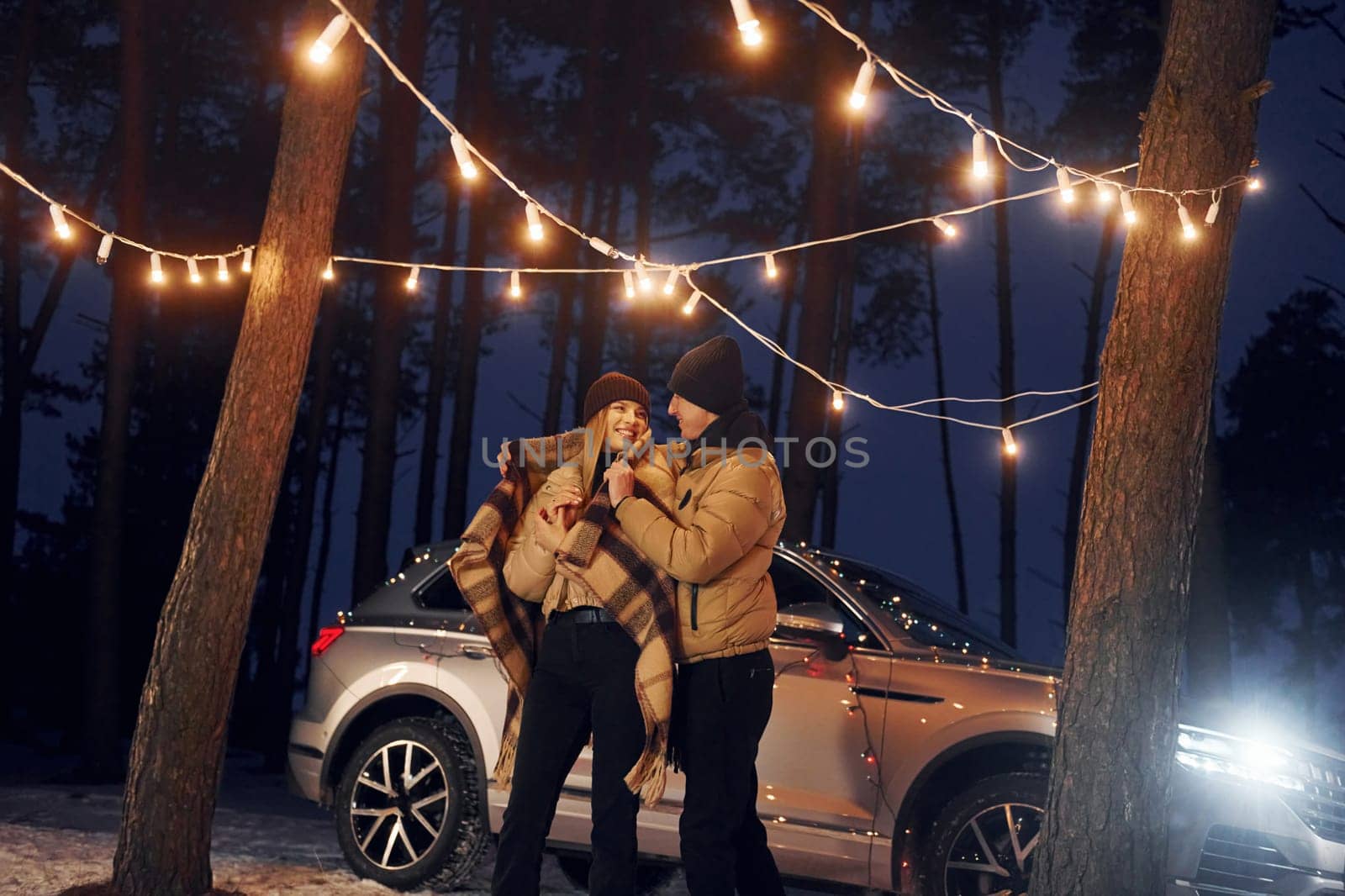 Car is at background. Couple standing in the forest and celebrating New year.