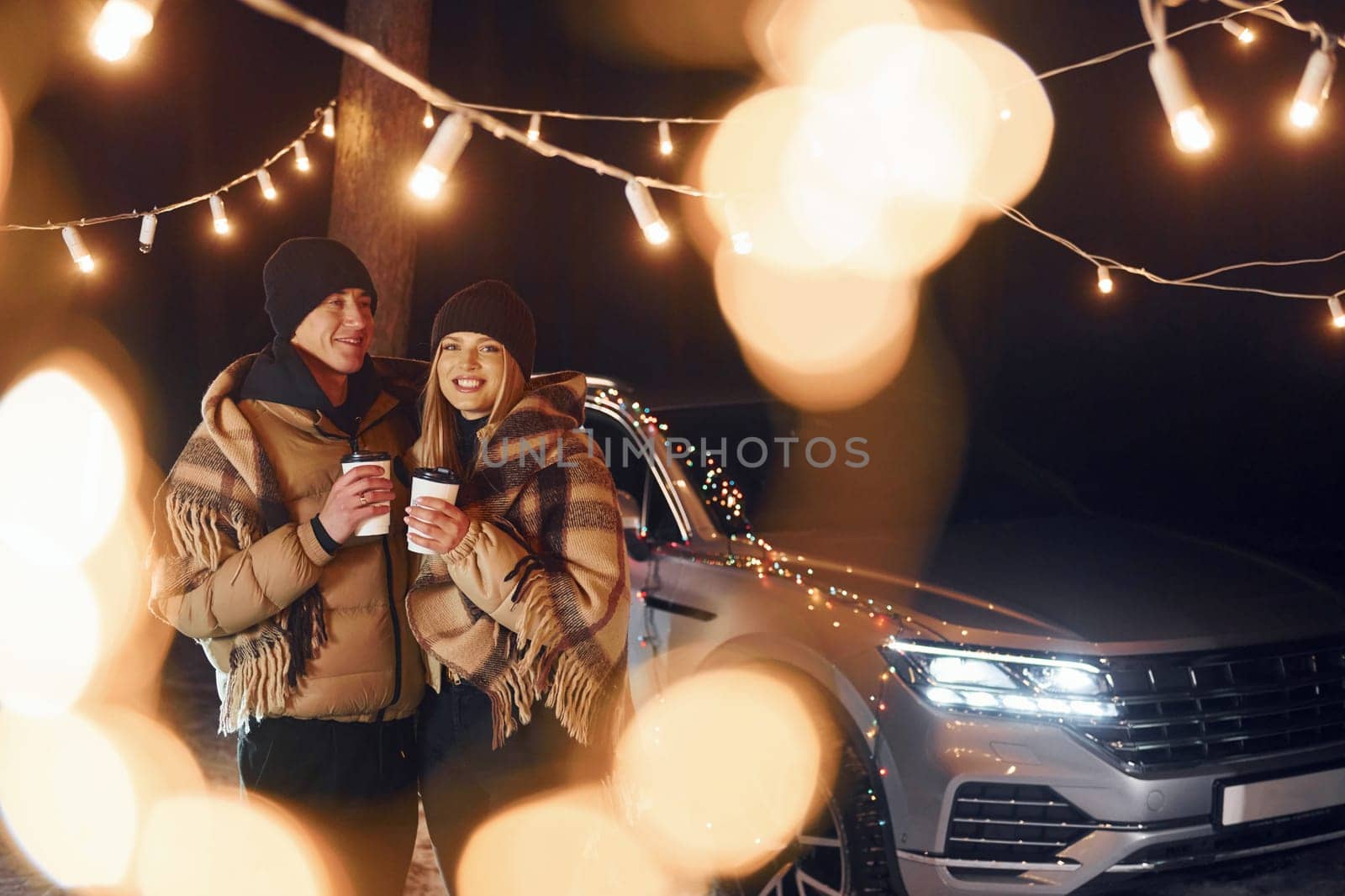 Standing near car. Couple is in the forest and celebrating New year.