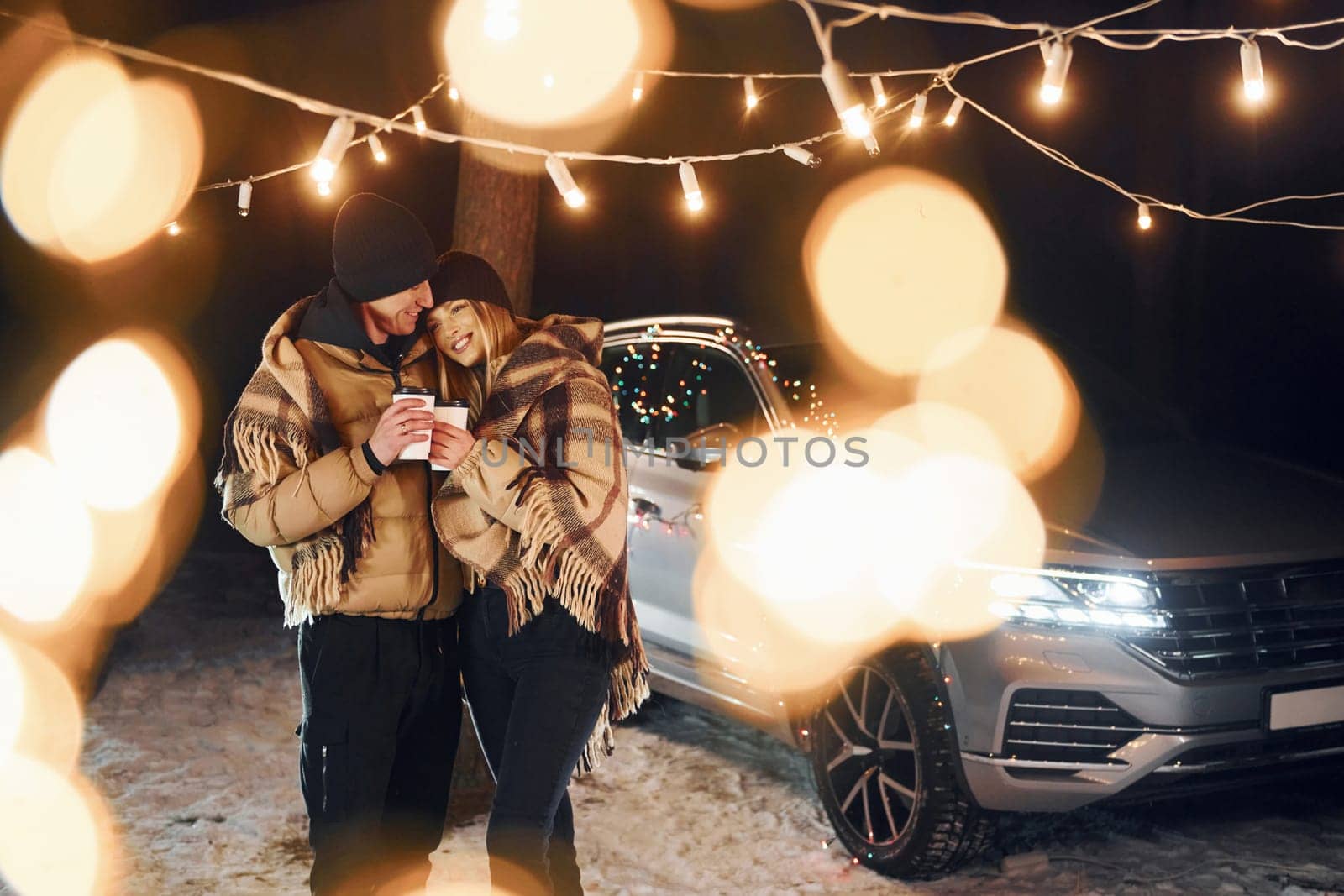 Standing near car. Couple is in the forest and celebrating New year.