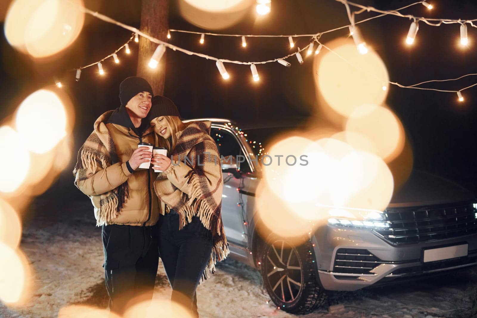 With warm drinks. Couple standing in the forest and celebrating New year.