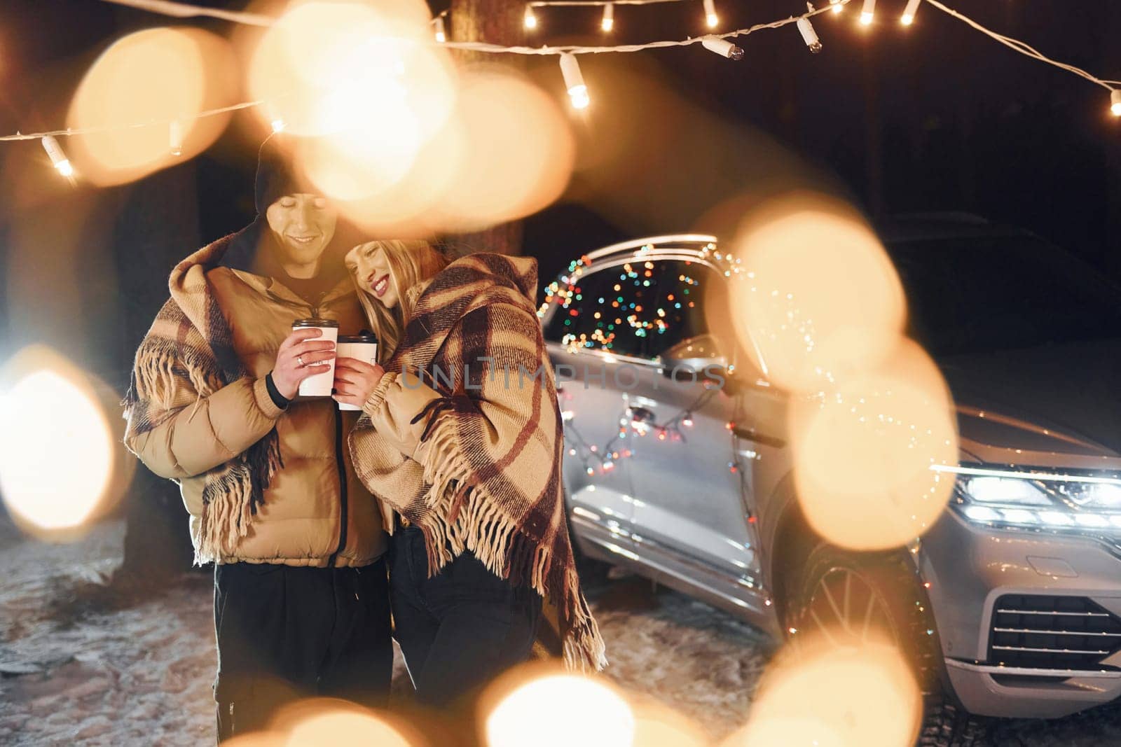 With warm drinks. Couple standing in the forest and celebrating New year.