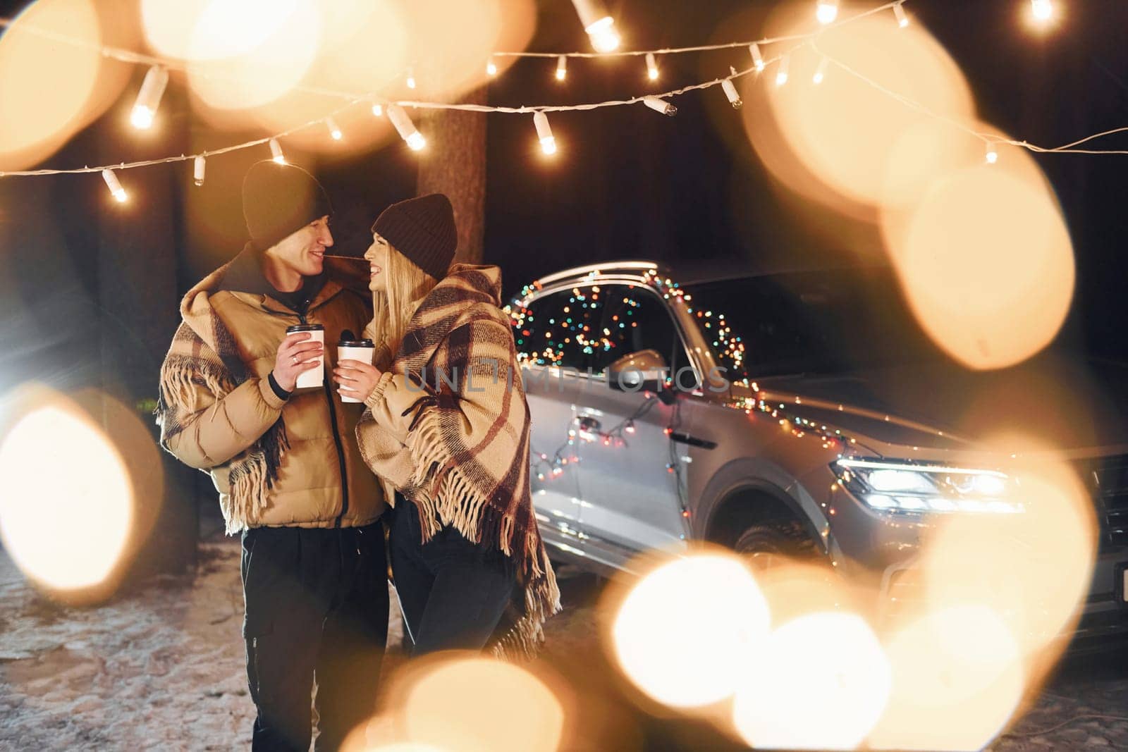With warm drinks. Couple standing in the forest and celebrating New year.