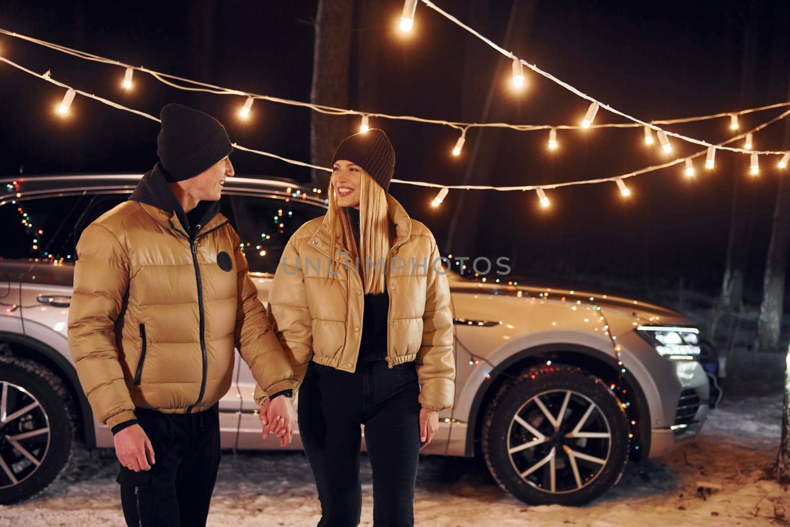 With modern car behind. Couple standing in the forest and celebrating New year.