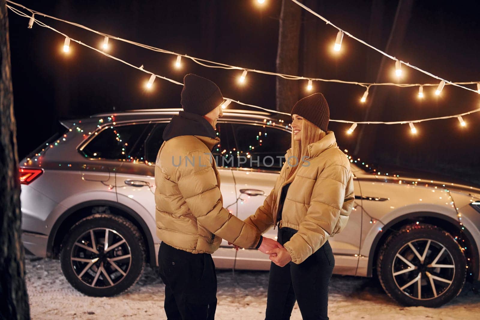 With modern car behind. Couple standing in the forest and celebrating New year.