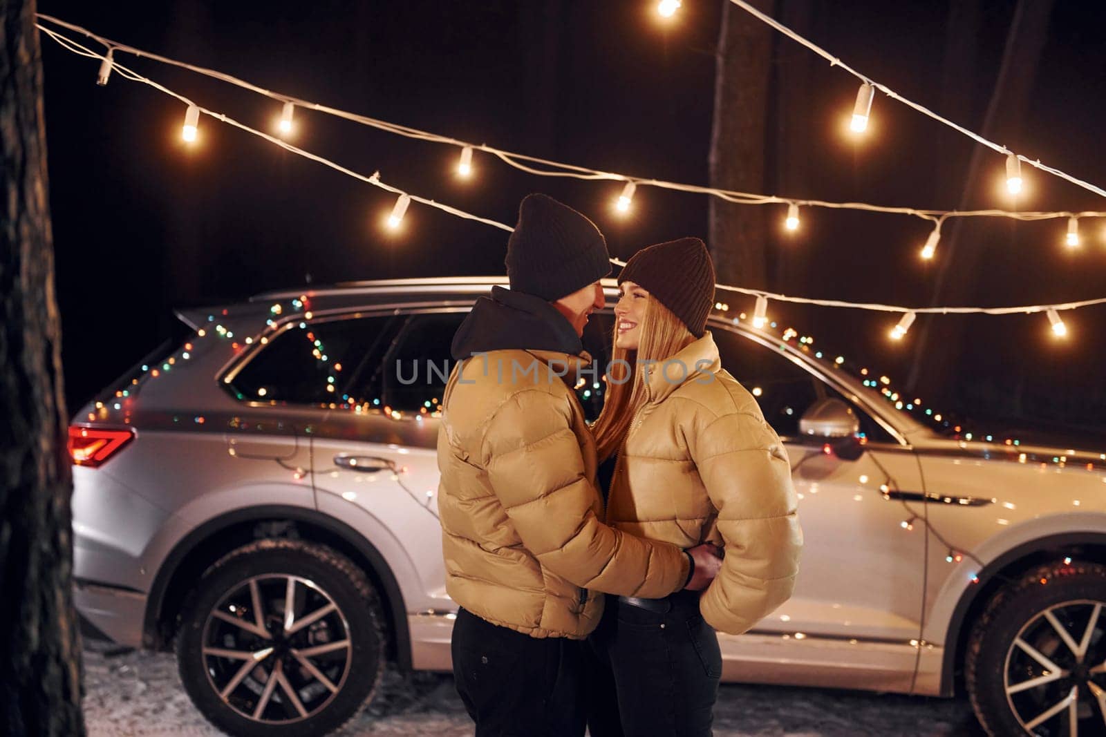 With modern car behind. Couple standing in the forest and celebrating New year.
