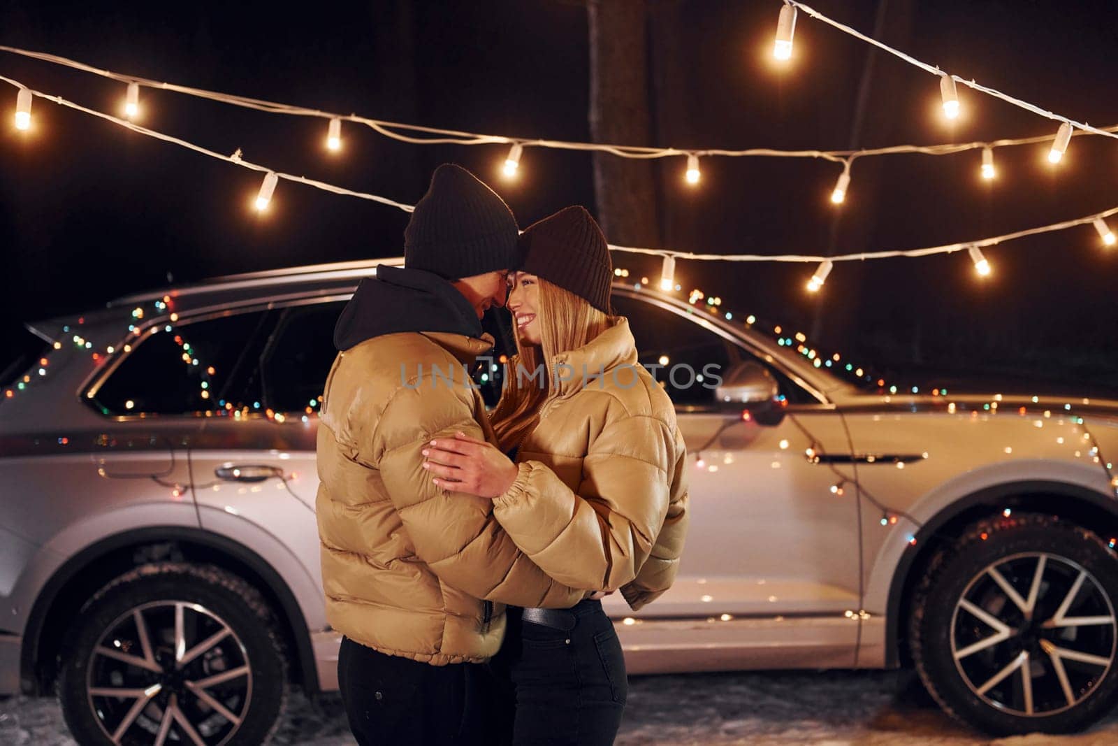 With modern car behind. Couple standing in the forest and celebrating New year.