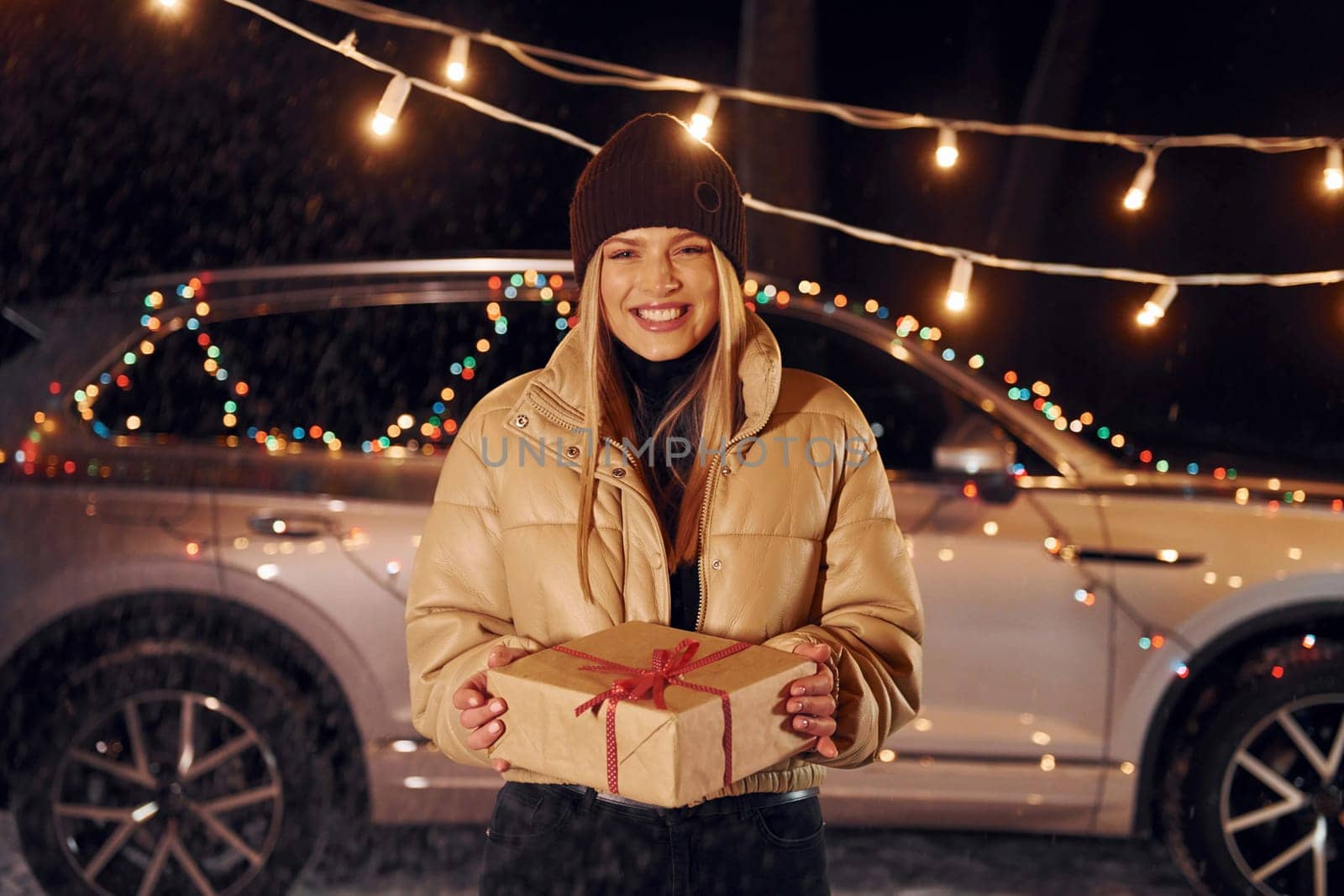 Smiling and holding gift. Woman standing in the forest and celebrating New year.