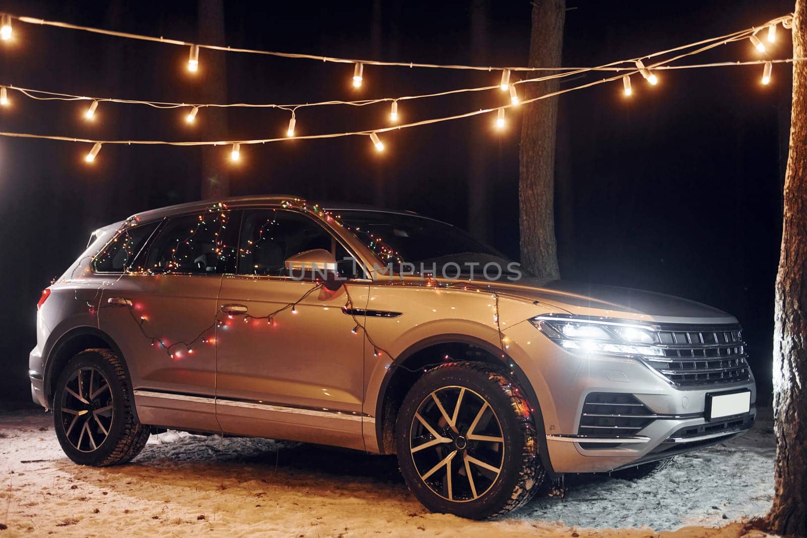 Modern silver colored automobile parked in forest with holiday decoration.