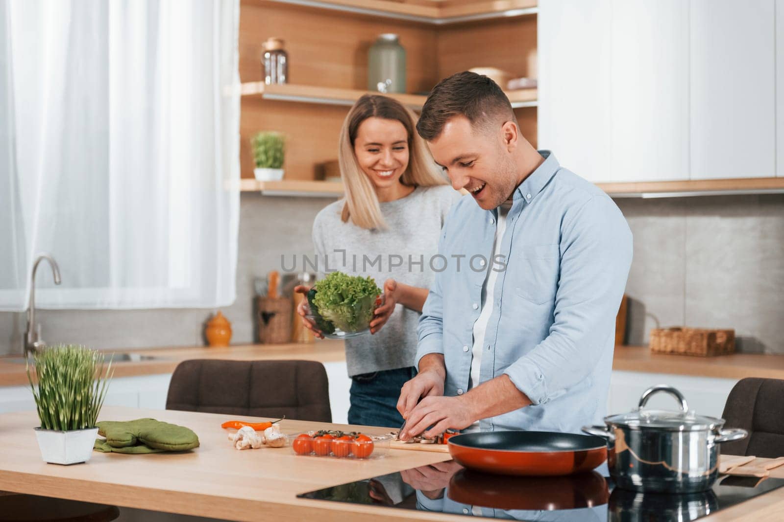 Man standing by the table. Couple preparing food at home on the modern kitchen by Standret