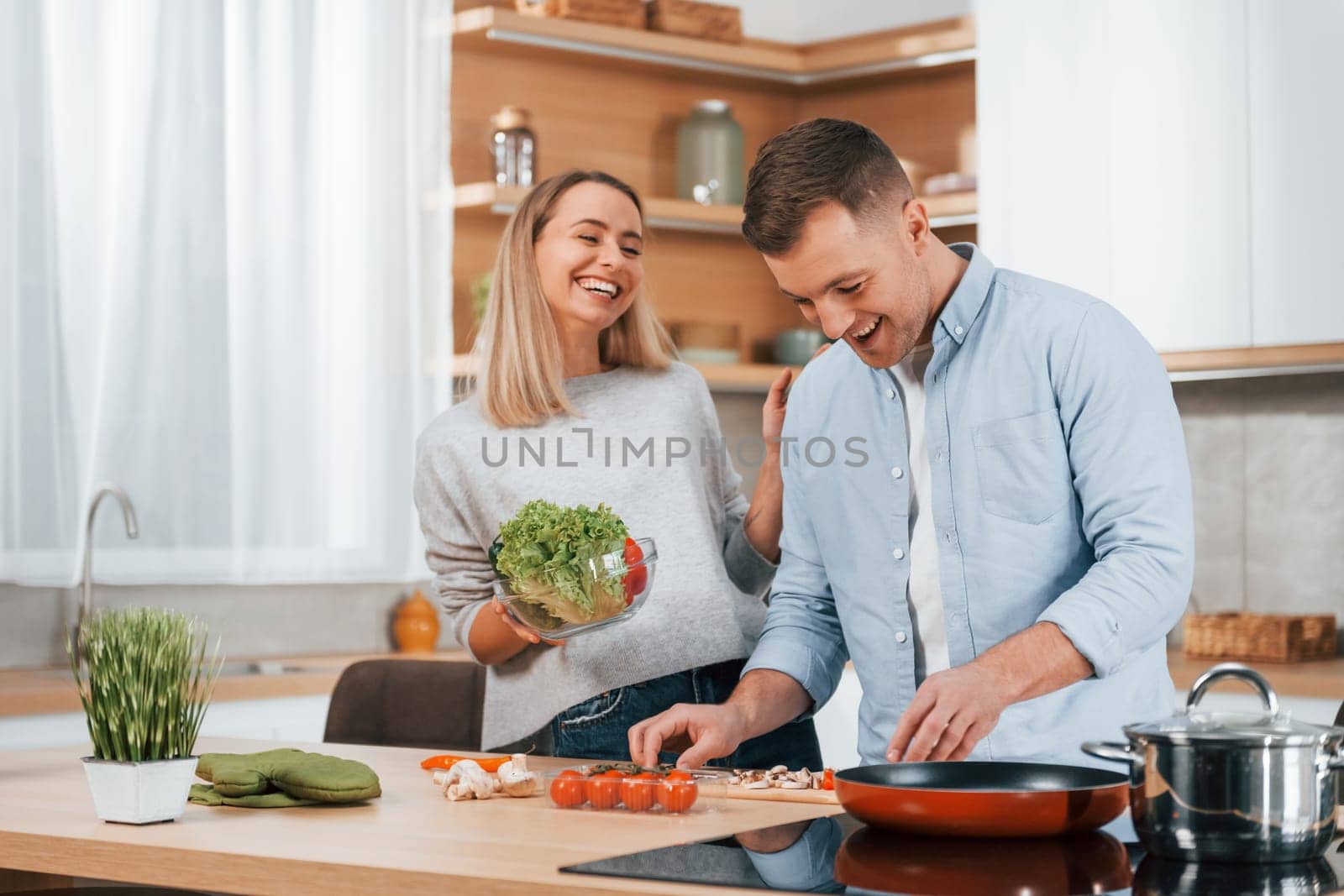 Man standing by the table. Couple preparing food at home on the modern kitchen by Standret