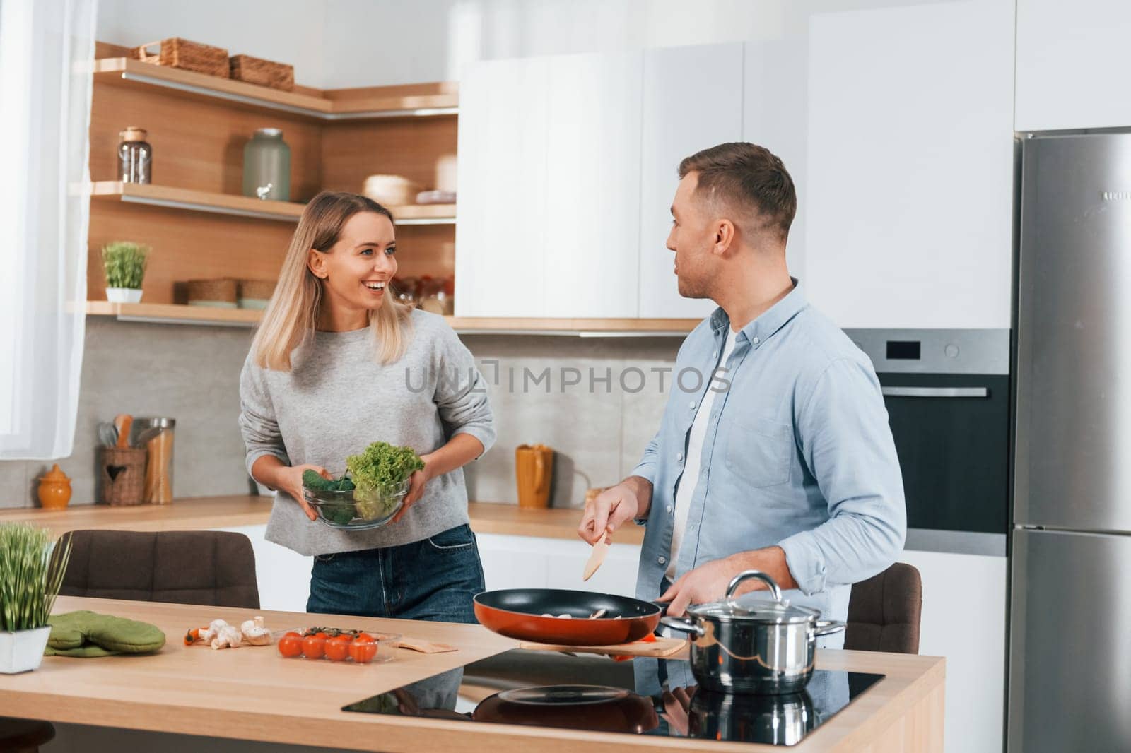 Talking with each other. Couple preparing food at home on the modern kitchen by Standret