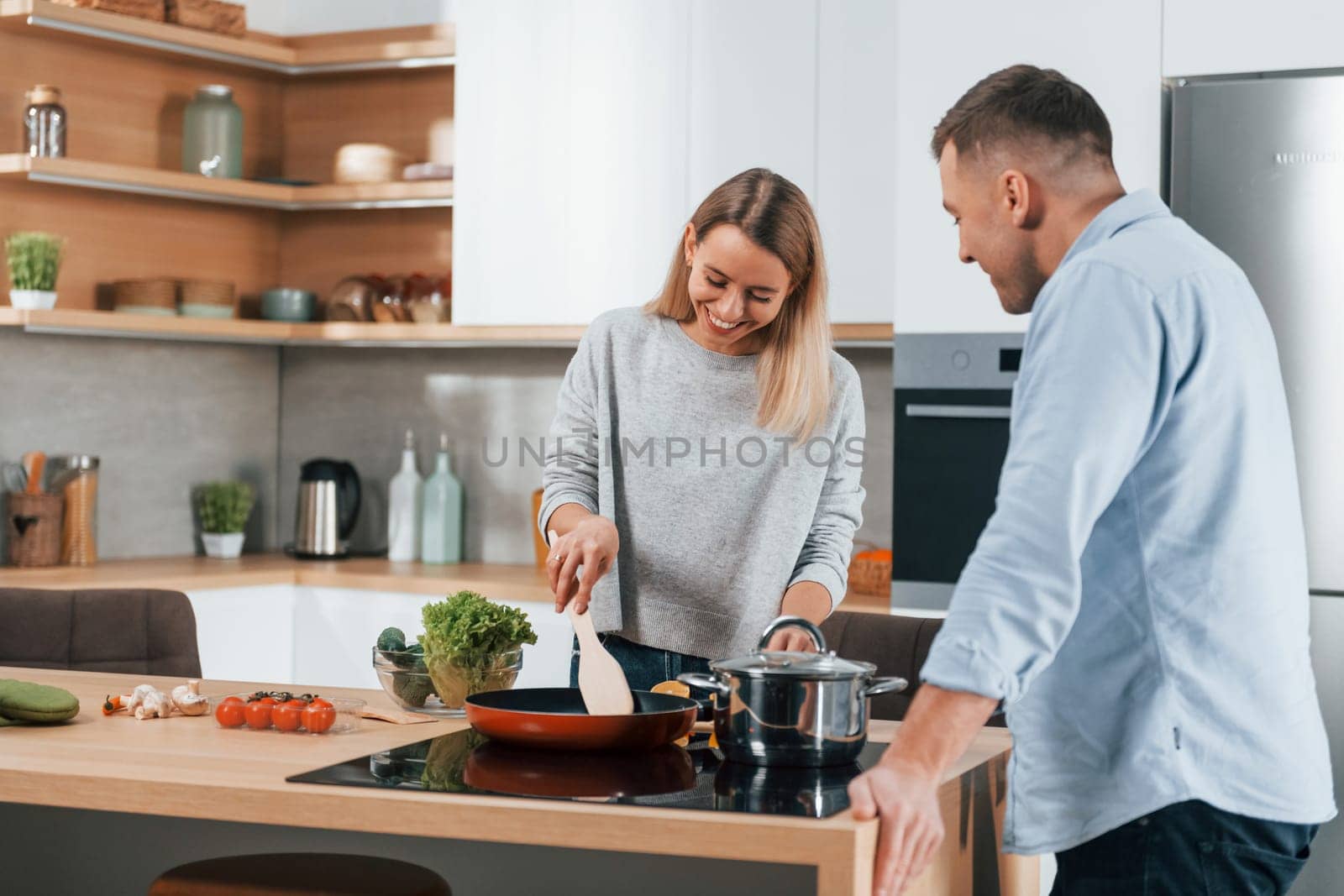 Delicious dinner. Couple preparing food at home on the modern kitchen by Standret