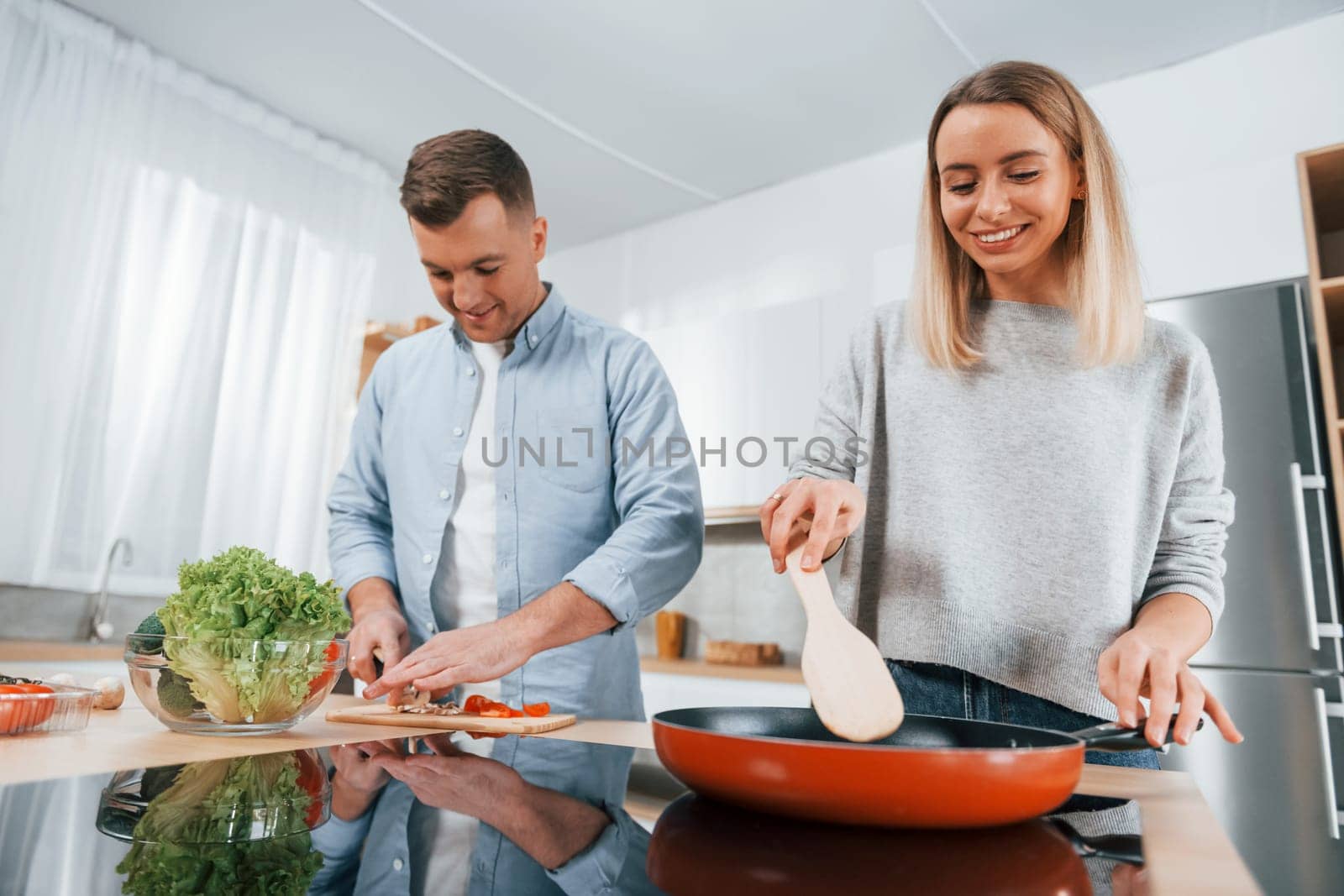 Frying food in a pan. Couple preparing food at home on the modern kitchen by Standret