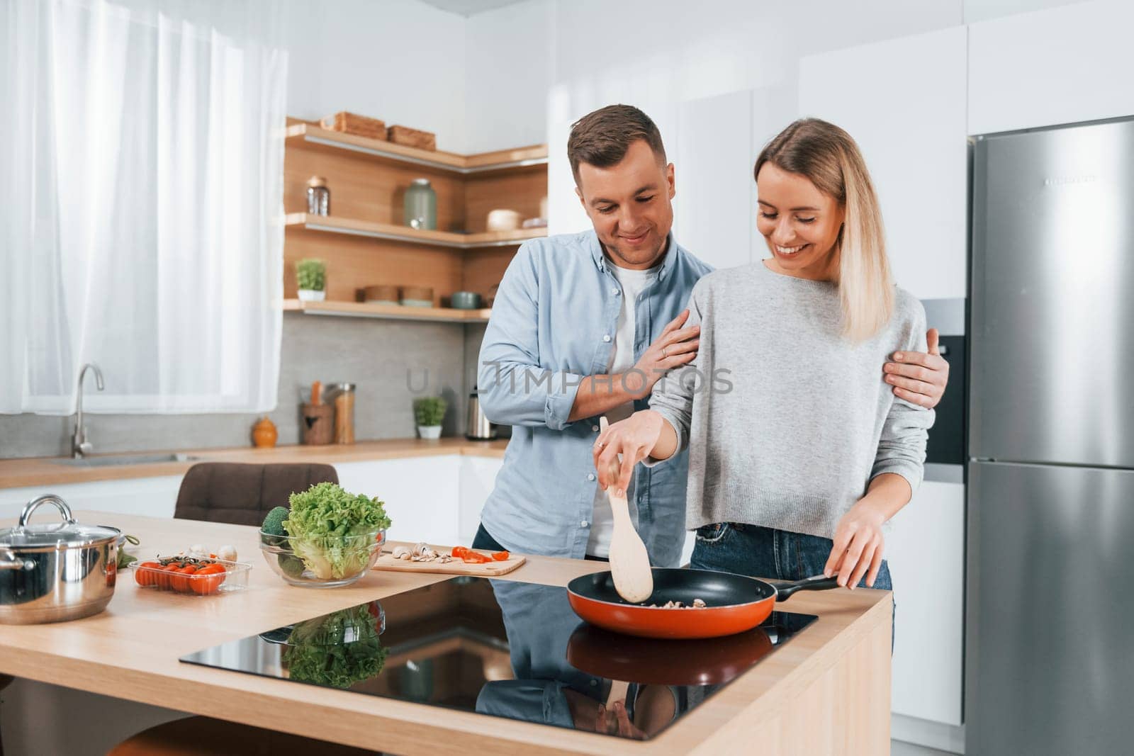 Frying food in a pan. Couple preparing food at home on the modern kitchen by Standret