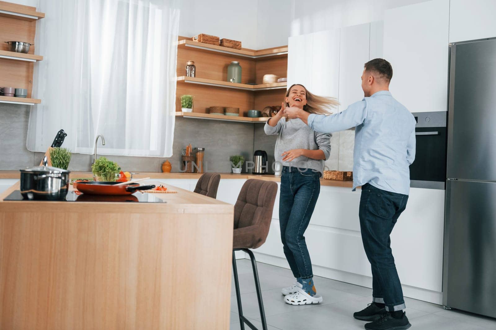 Dancing together. Couple preparing food at home on the modern kitchen by Standret