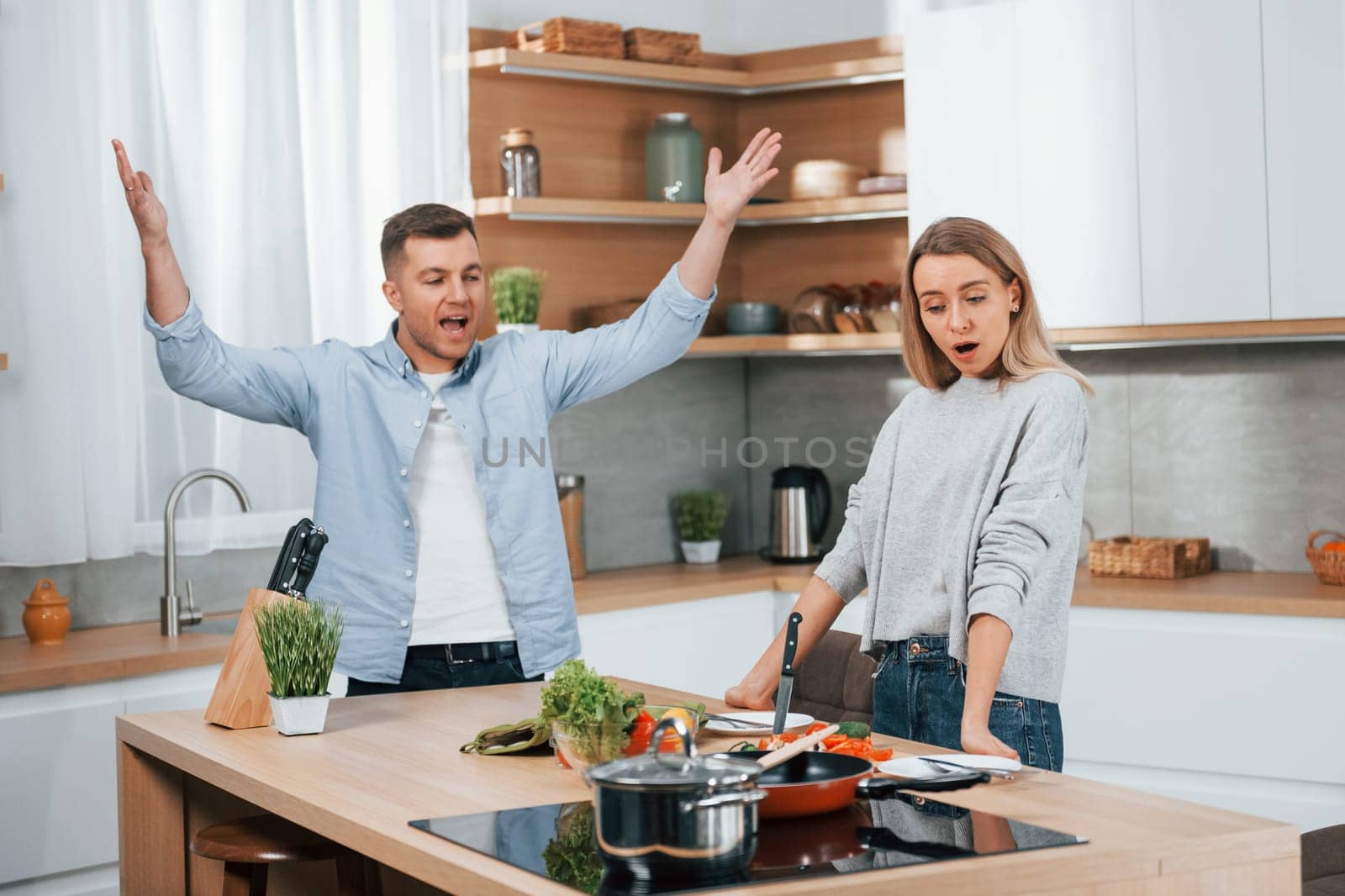Arguing with each other. Couple preparing food at home on the modern kitchen by Standret