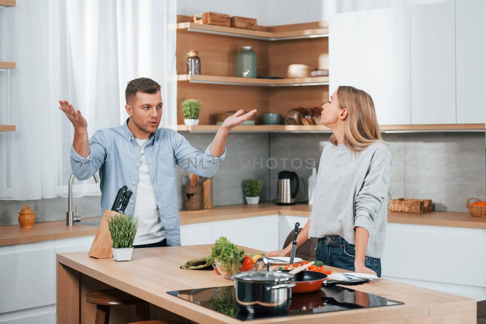 Screaming and arguing with each other. Couple preparing food at home on the modern kitchen by Standret