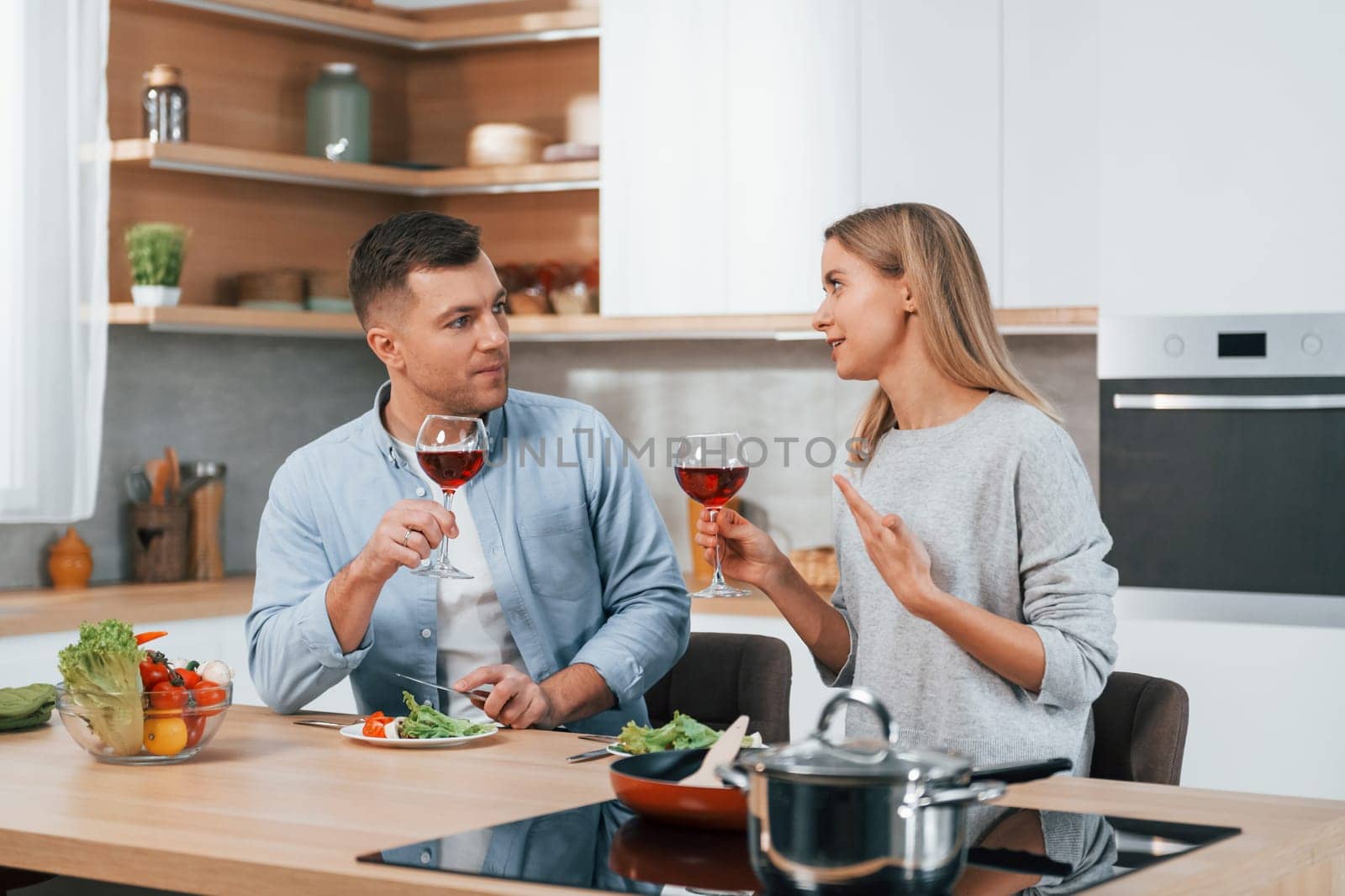 With glasses of wine. Couple preparing food at home on the modern kitchen by Standret