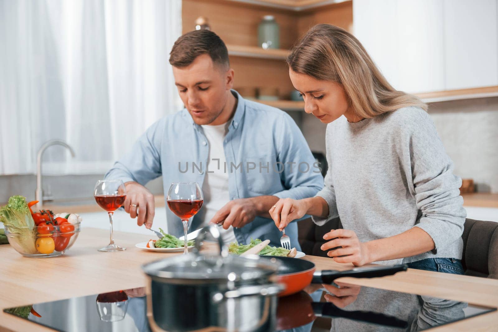 With glasses of wine. Couple preparing food at home on the modern kitchen by Standret