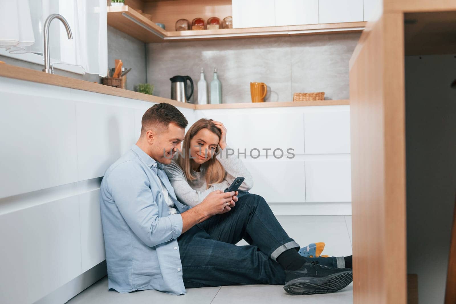 Couple sitting on the floor of modern kitchen by Standret