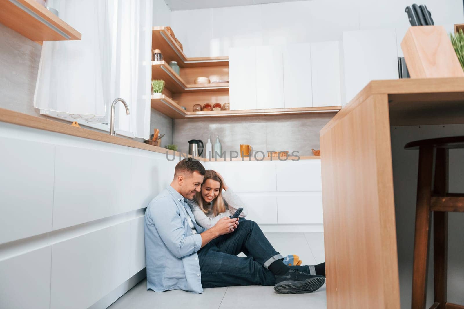 Couple sitting on the floor of modern kitchen by Standret