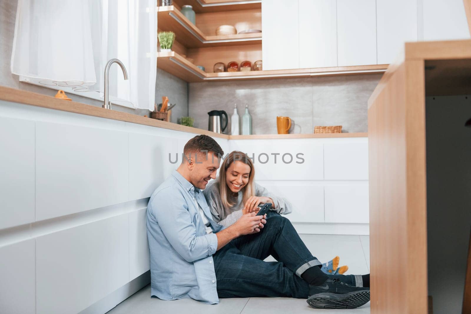 Couple sitting on the floor of modern kitchen.