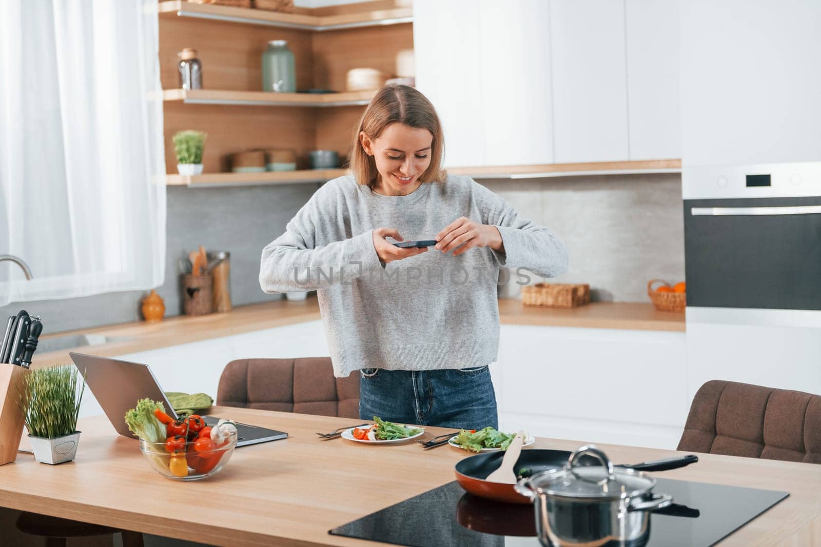 Taking pictures. Woman preparing food at home on the modern kitchen by Standret