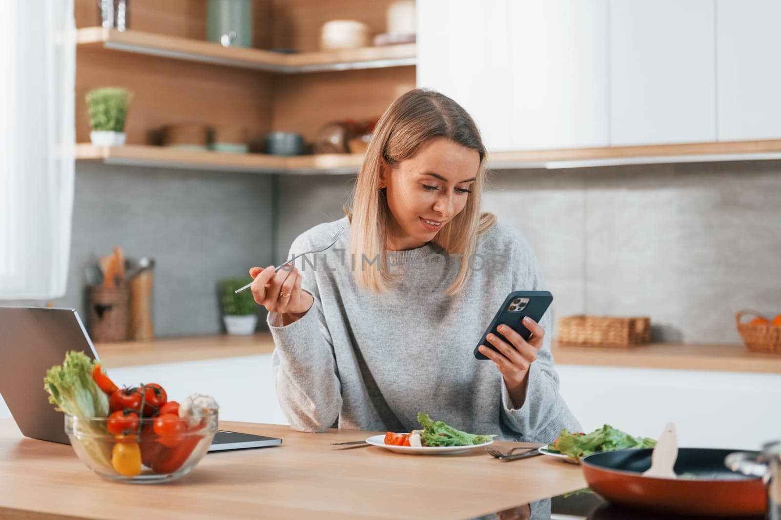 Holding phone. Woman preparing food at home on the modern kitchen.