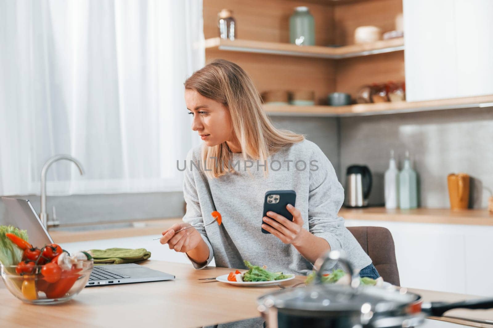 Holding phone. Woman preparing food at home on the modern kitchen by Standret