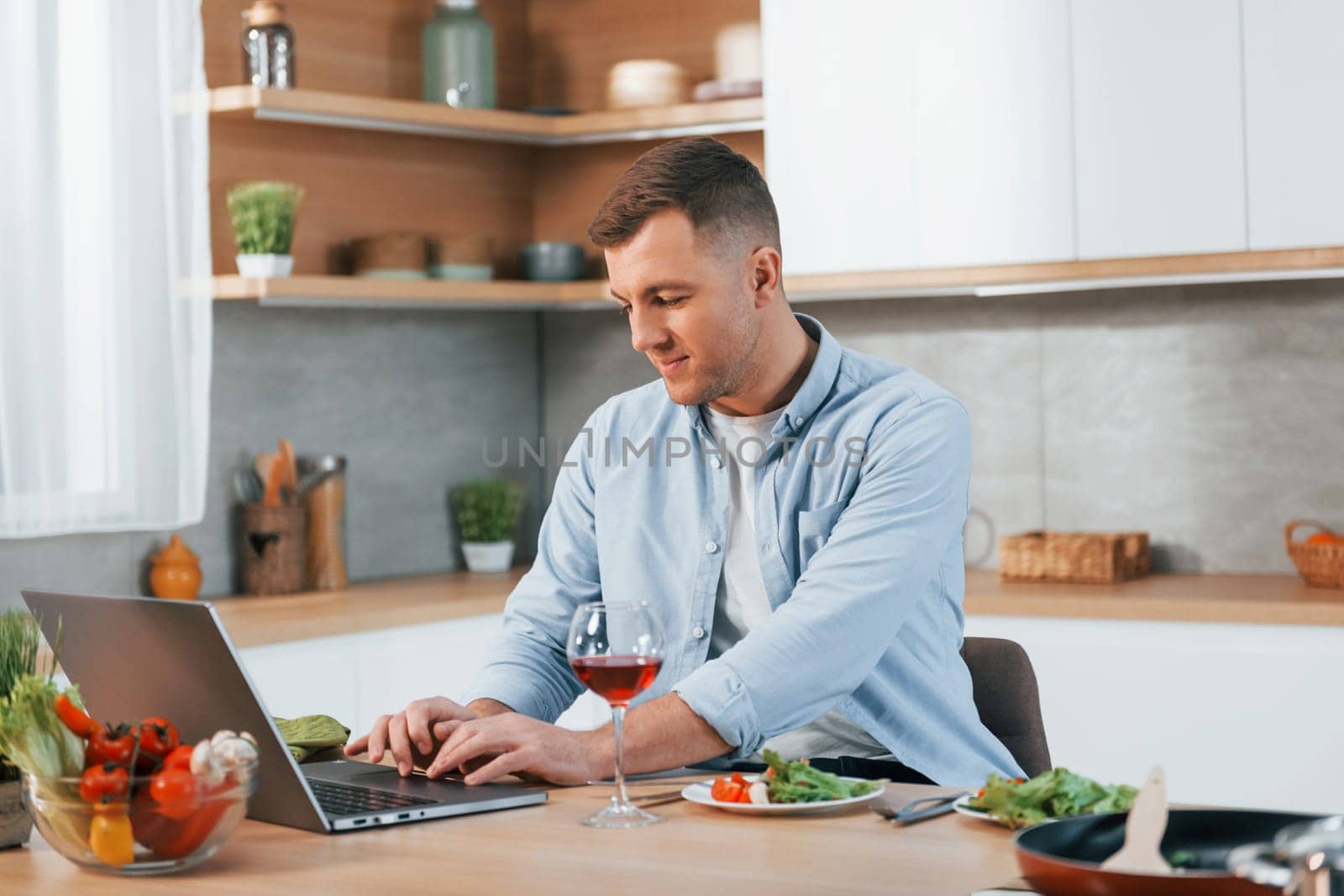 Using laptop. Man preparing food at home on the modern kitchen.