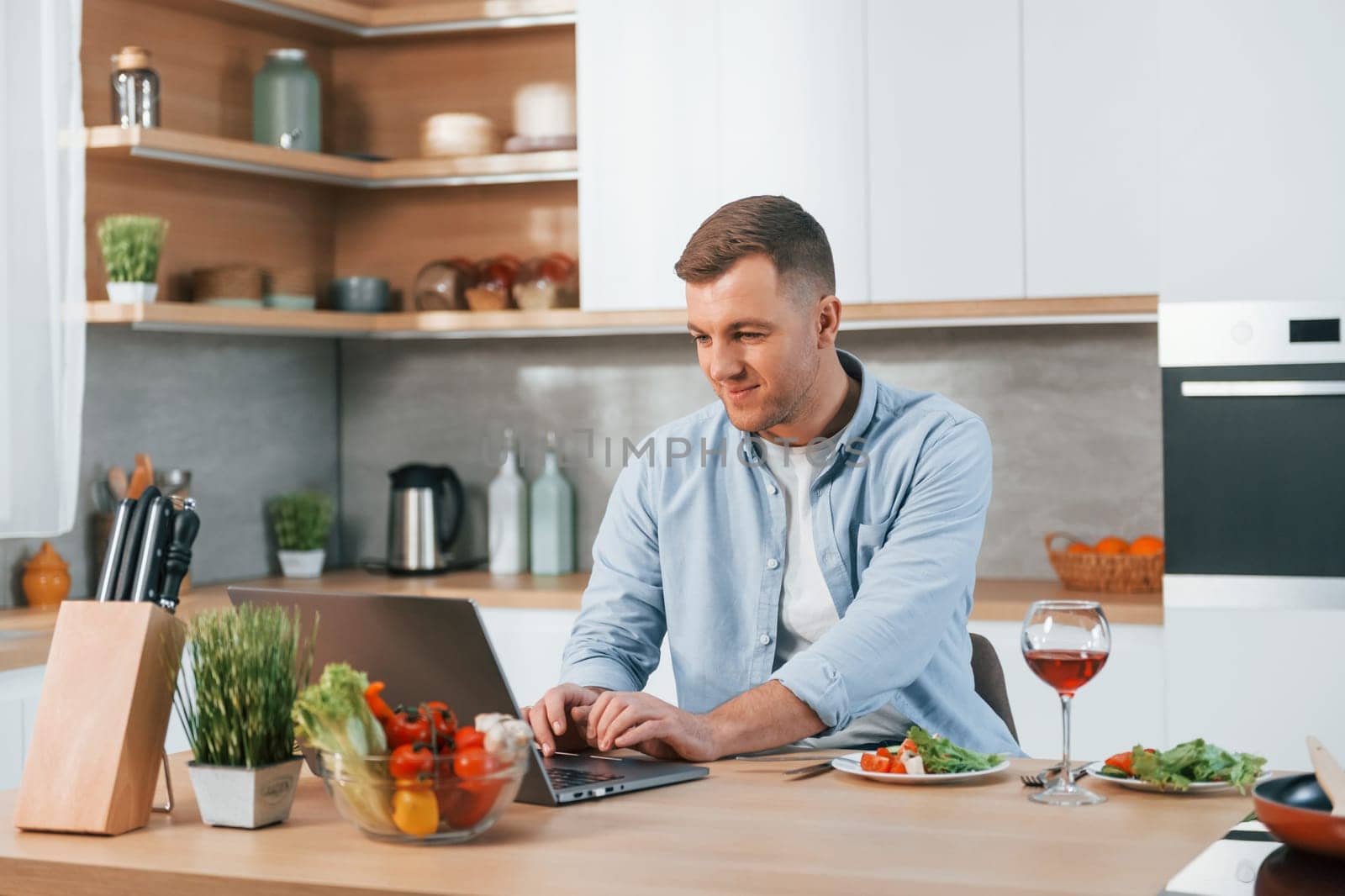 Using laptop. Man preparing food at home on the modern kitchen.