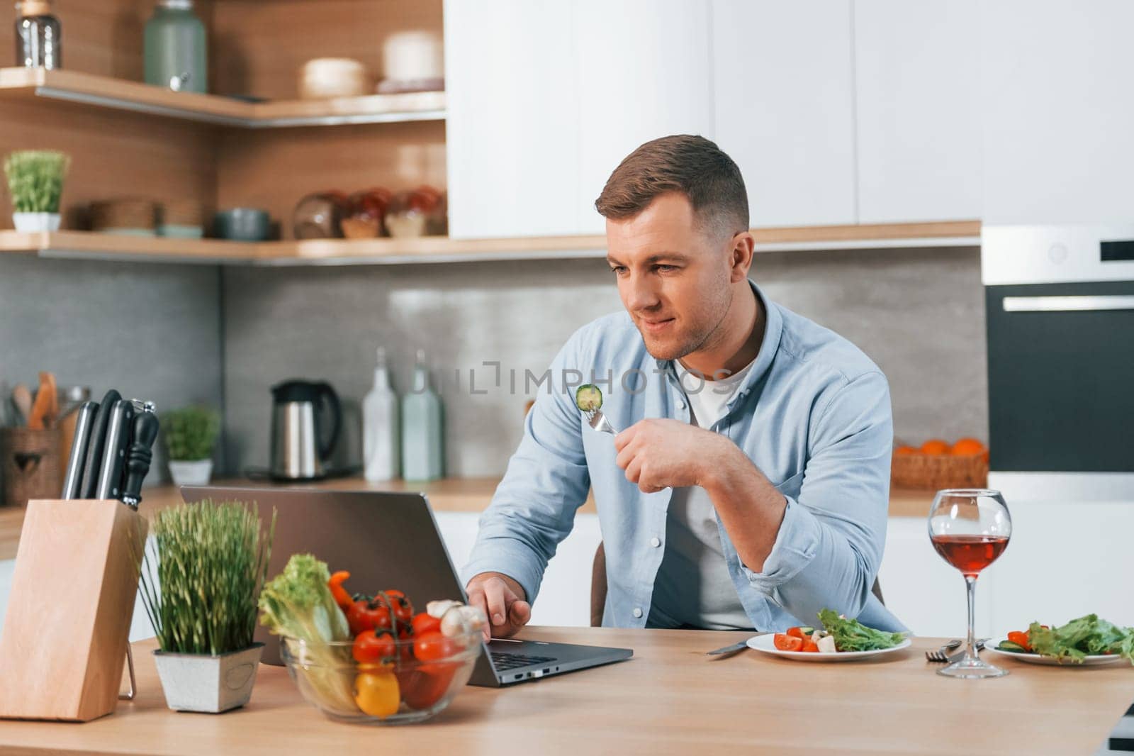 Using laptop. Man preparing food at home on the modern kitchen.