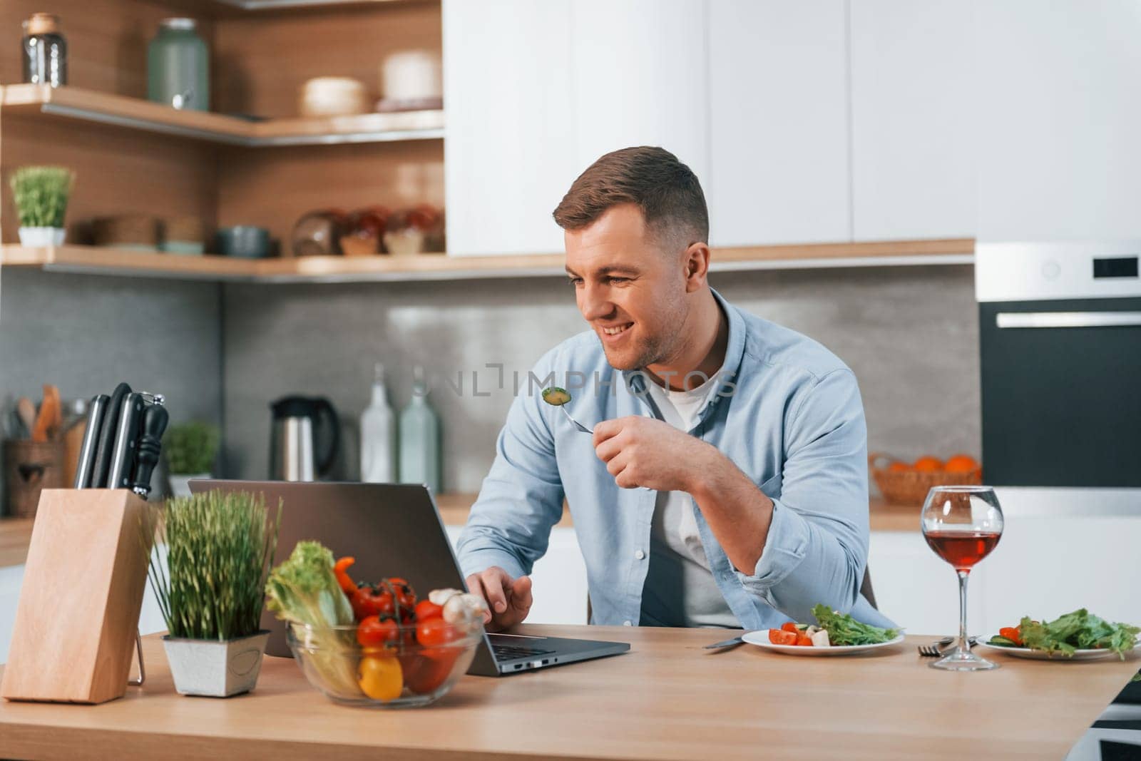 Using laptop. Man preparing food at home on the modern kitchen.