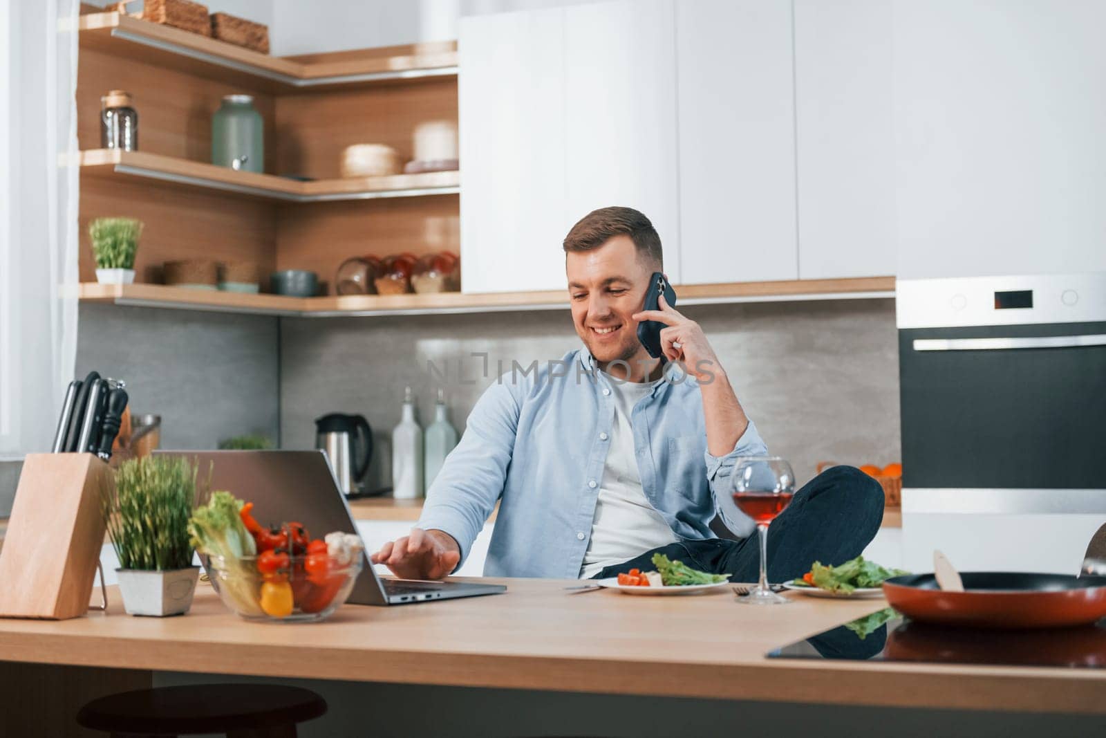 Talking by phone. Man preparing food at home on the modern kitchen.