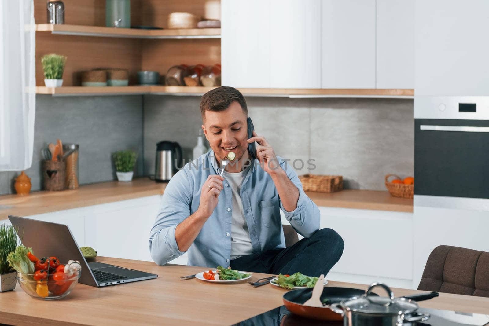 Talking by phone. Man preparing food at home on the modern kitchen.