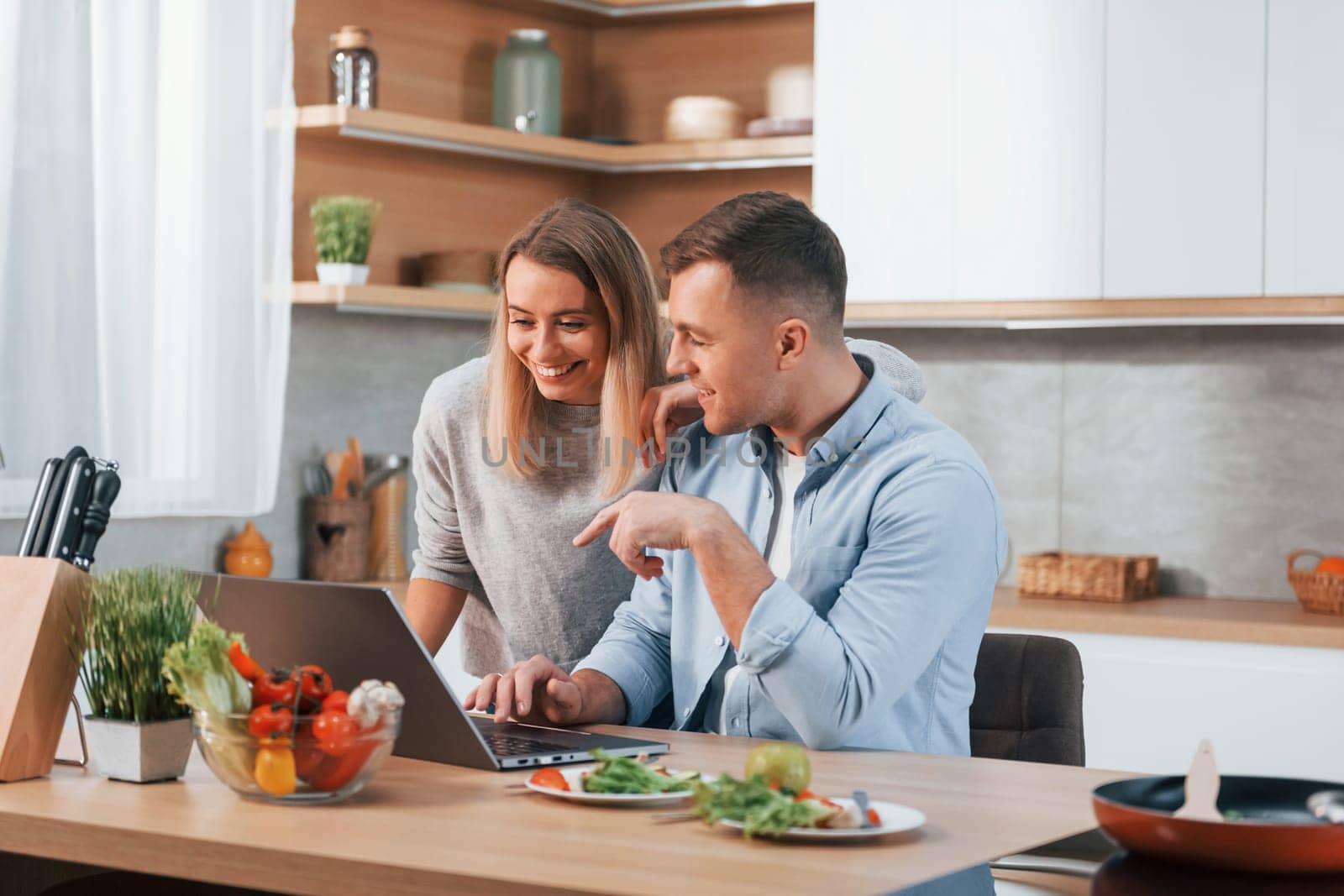 Looking at laptop. Couple preparing food at home on the modern kitchen.