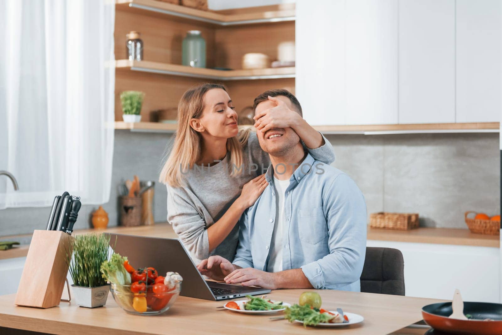 Laptop is on the table. Couple preparing food at home on the modern kitchen.