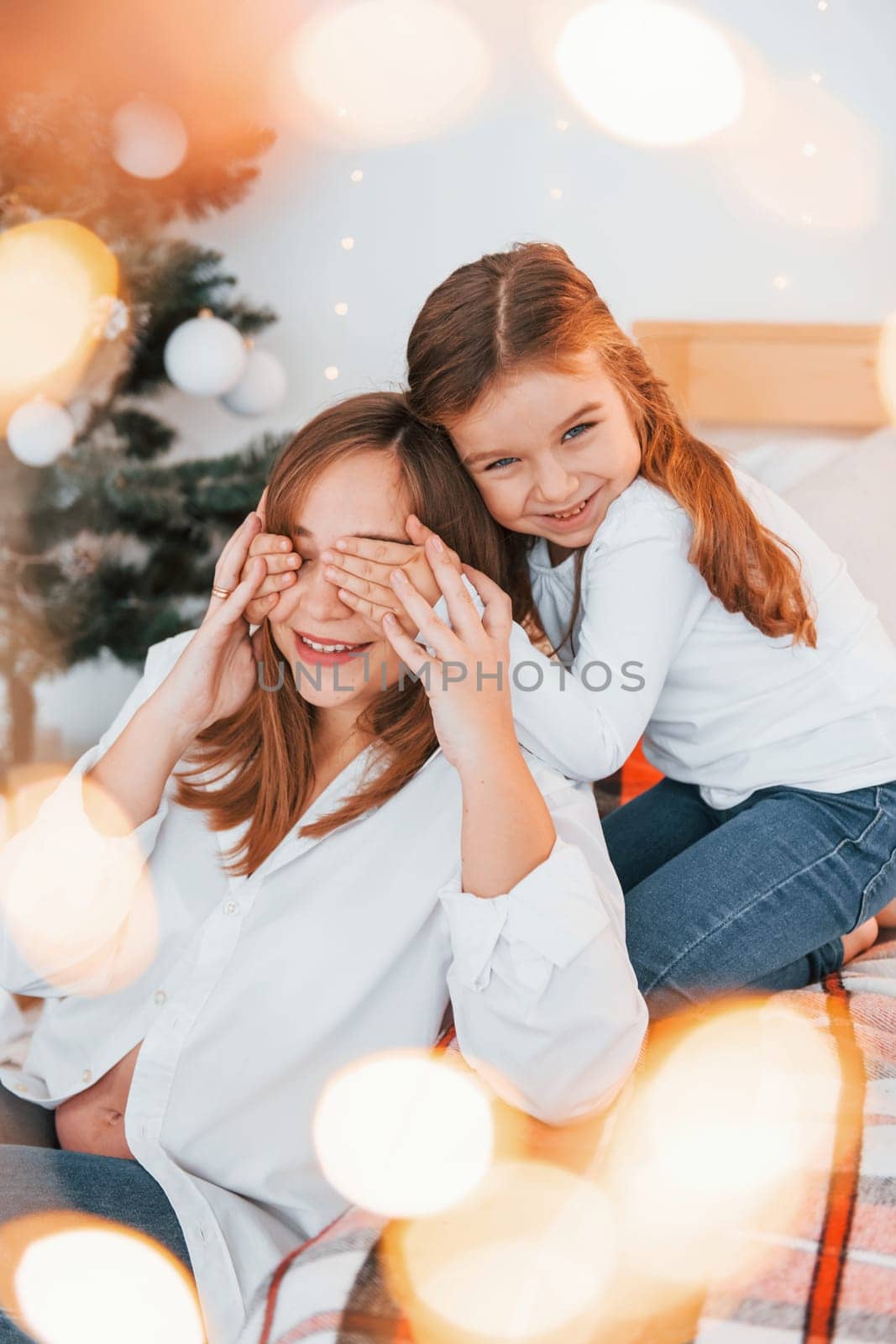 Mother with her little daughter is having fun indoors on the bed.